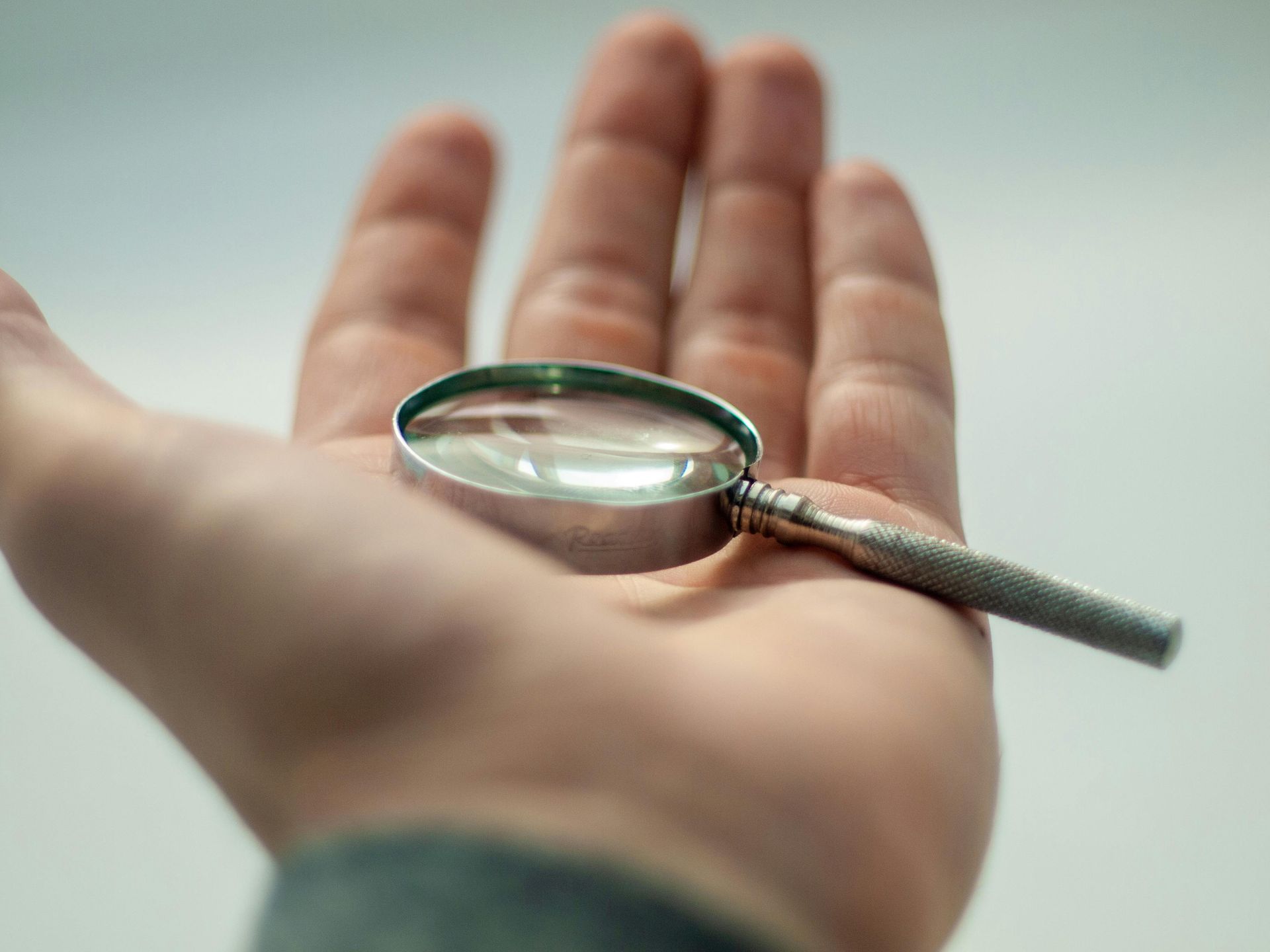 Hand die een klein vergrootglas vasthoudt, met de handpalm naar boven, tegen een witte achtergrond.