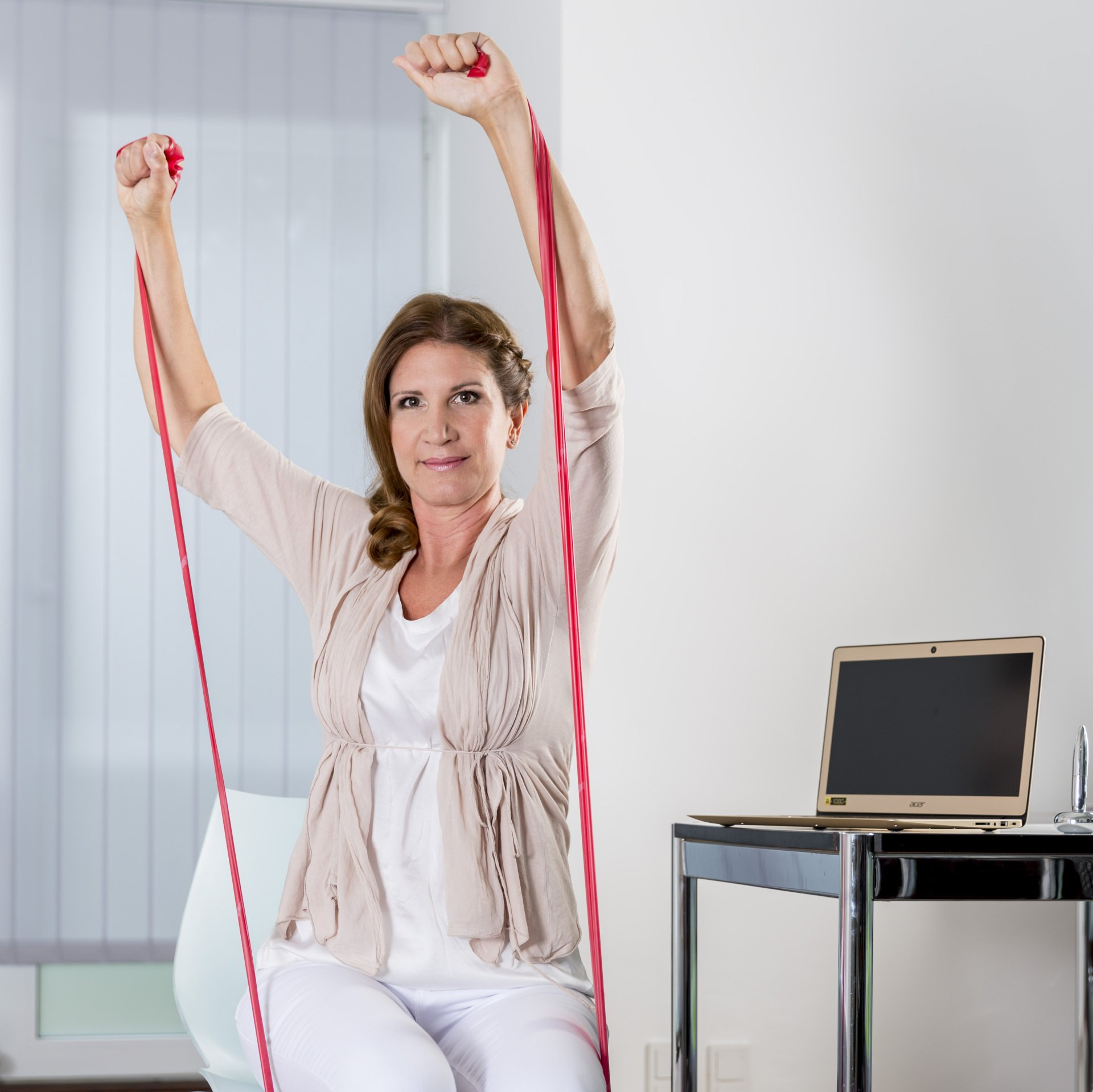 Eine Frau sitzt auf einem Stuhl und hält ein rotes Widerstandsband.