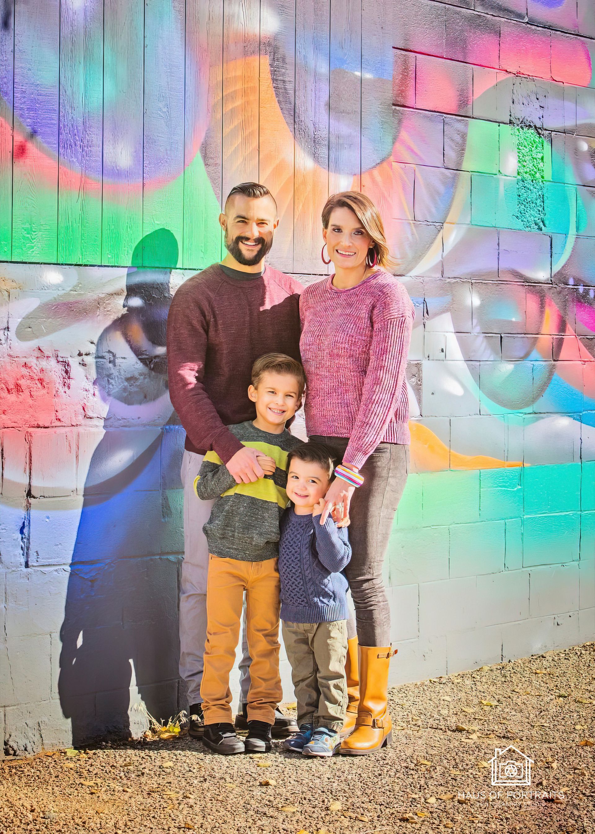 Family of four posing in front of a colorful mural with a graffiti artist's portrait.