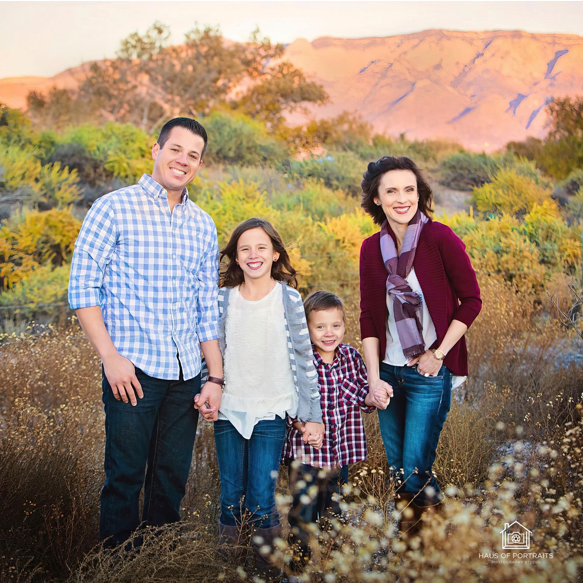 Family of four posing outdoors in a desert landscape with mountains and wildflowers at sunset