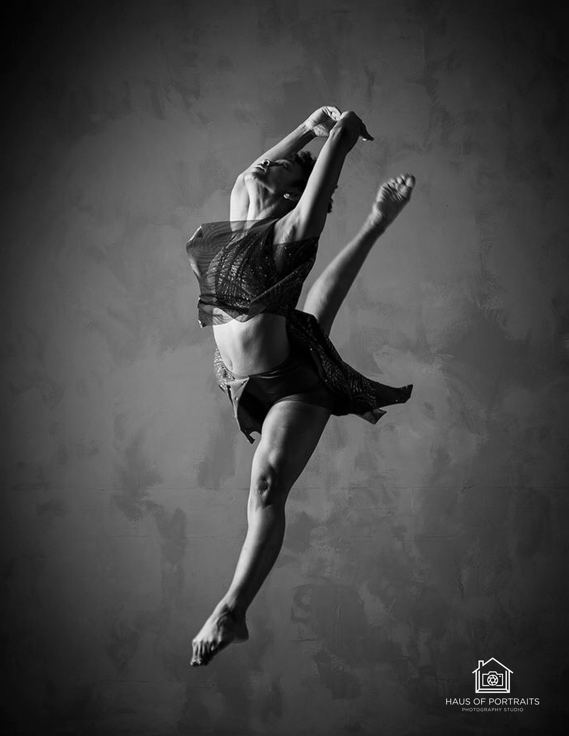 Black-and-white photo of a dancer midair in a graceful leap against a plain studio backdrop