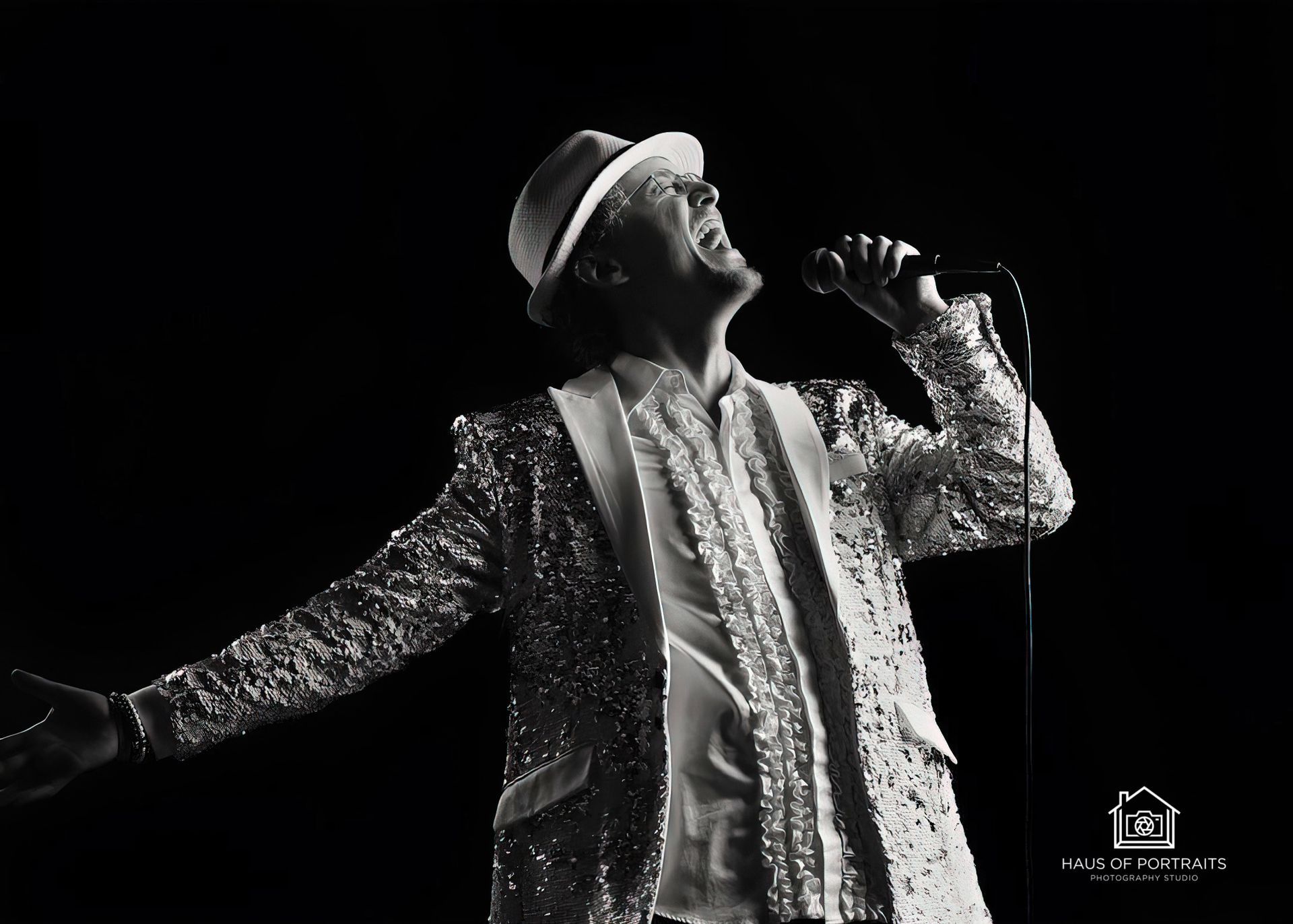 Singer in a glittering coat and hat performing with a microphone on a dark stage