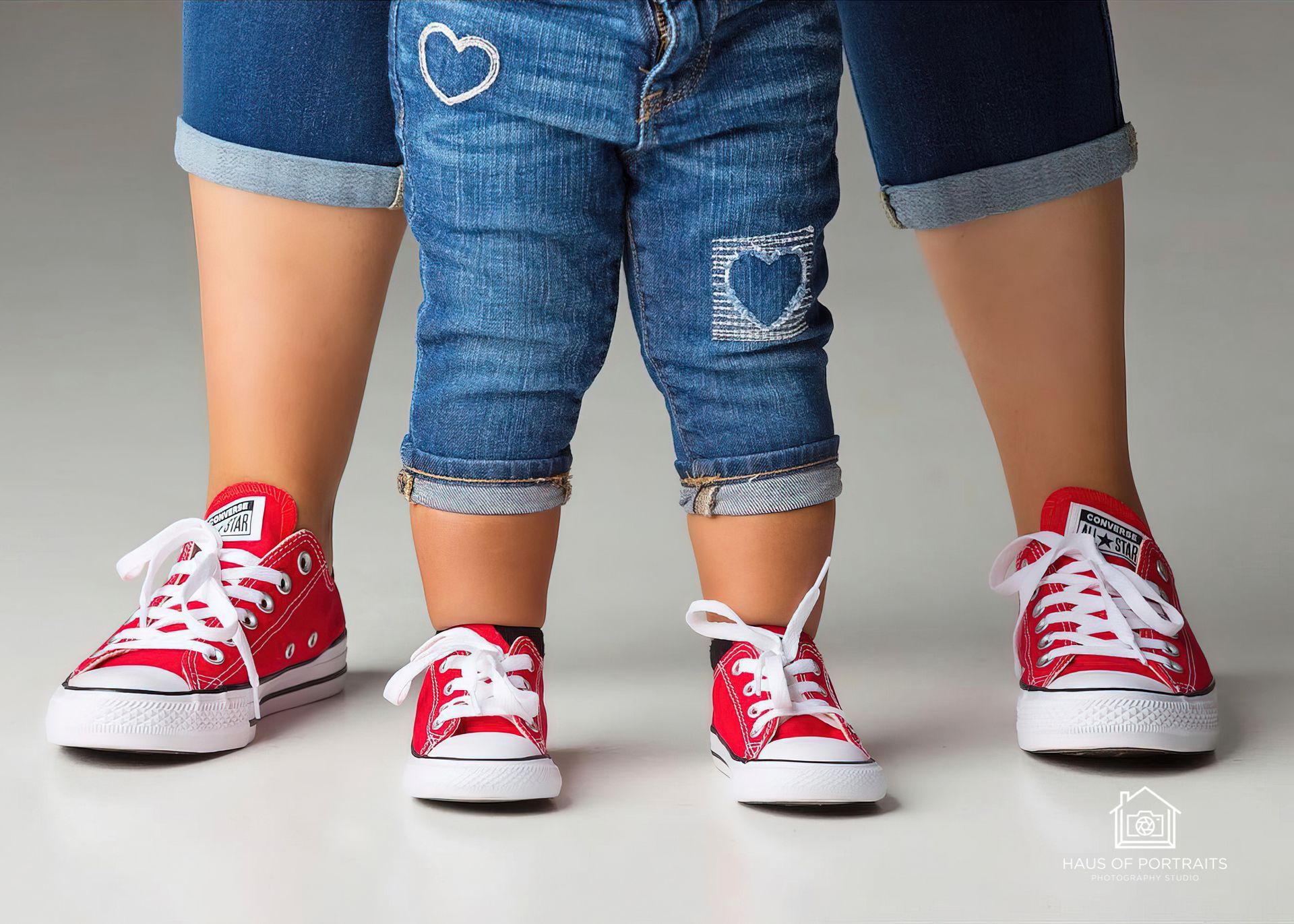 Three people standing close together, wearing matching red sneakers and denim outfits with heart patches.