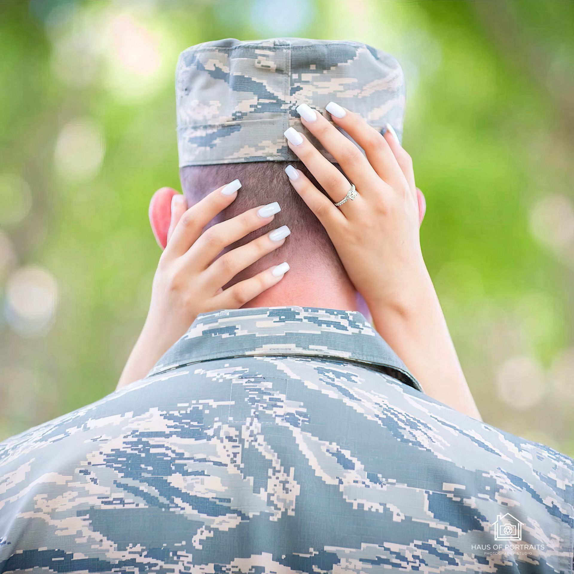 Hands with French manicure resting on a camouflage-uniformed soldier's neck outdoors