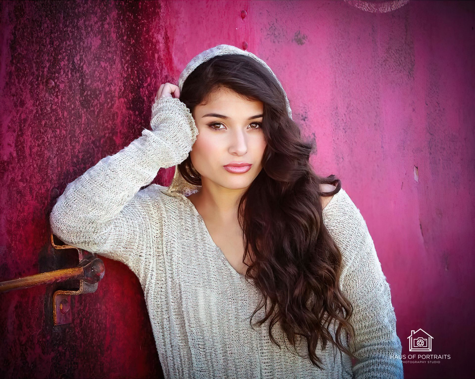 Woman in a light sweater and knit hat leaning against a pink textured wall