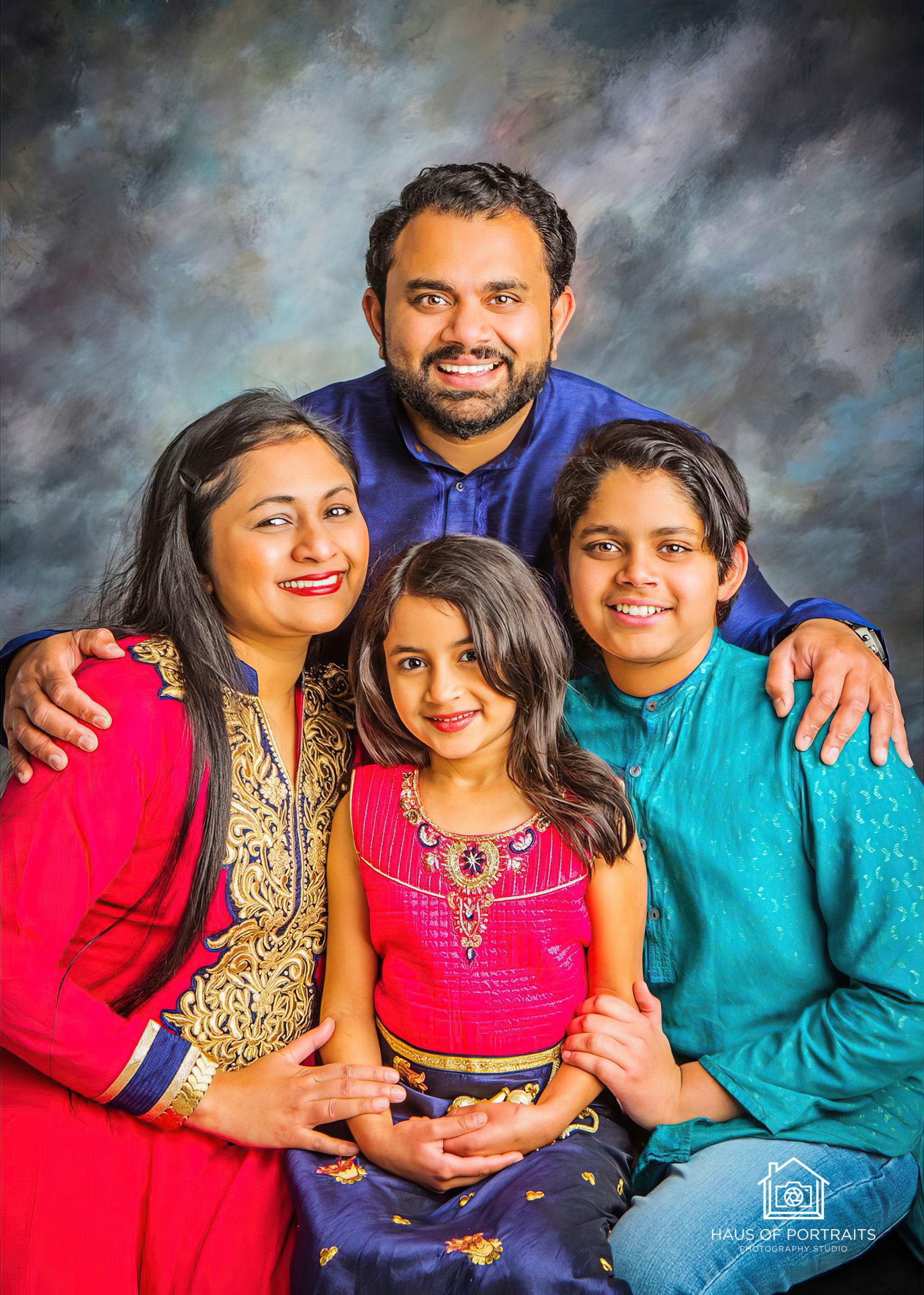 Family portrait of four posing together against a gray studio backdrop, smiling and seated close together