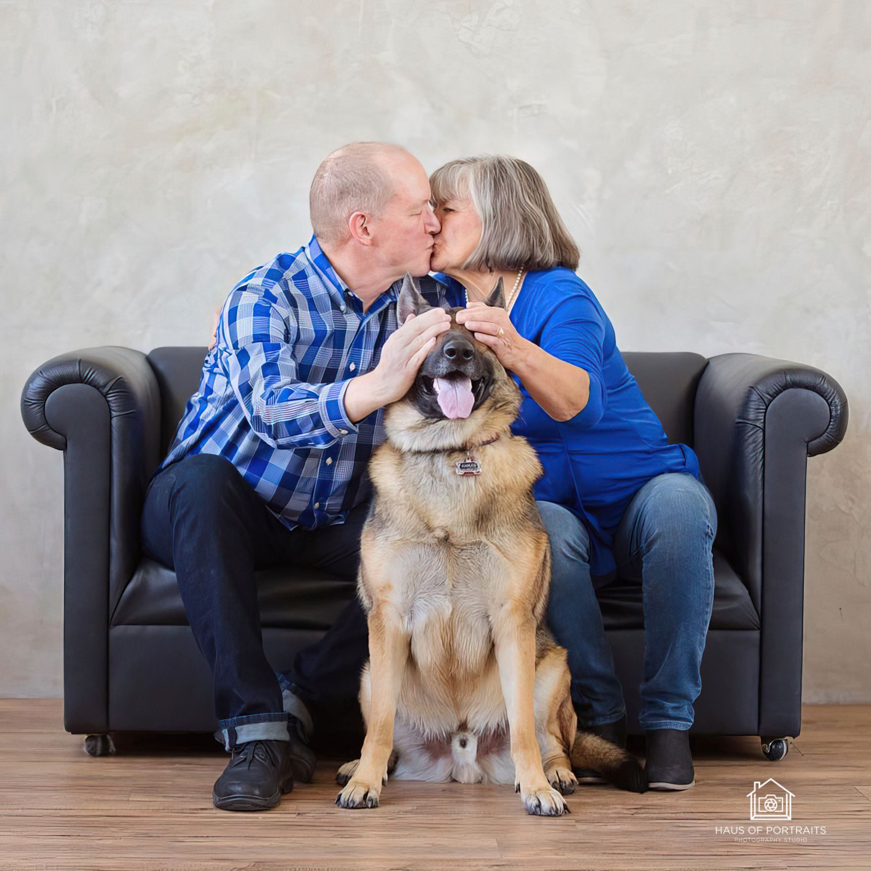 Older couple kissing on a couch with their large dog sitting between them