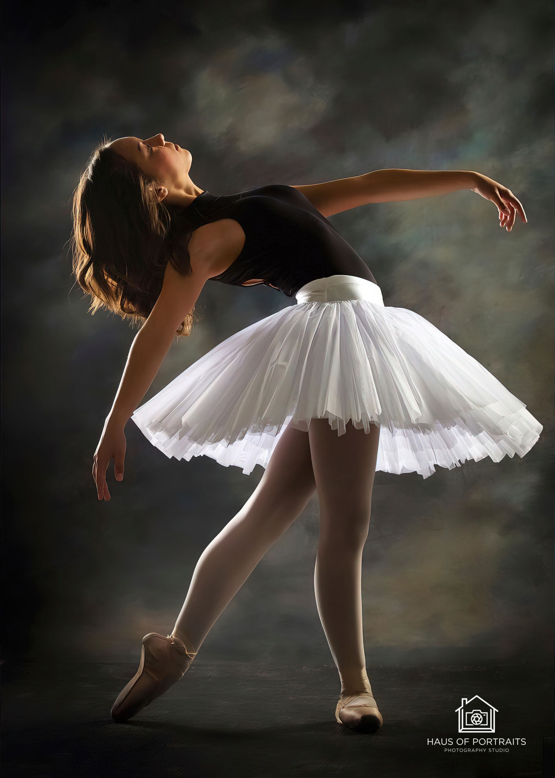 Ballet dancer in a white tutu leans back in a graceful pose against a dark studio backdrop