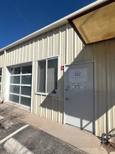 Exterior of beige industrial building with a garage door and gray utility cabinet in sunlight