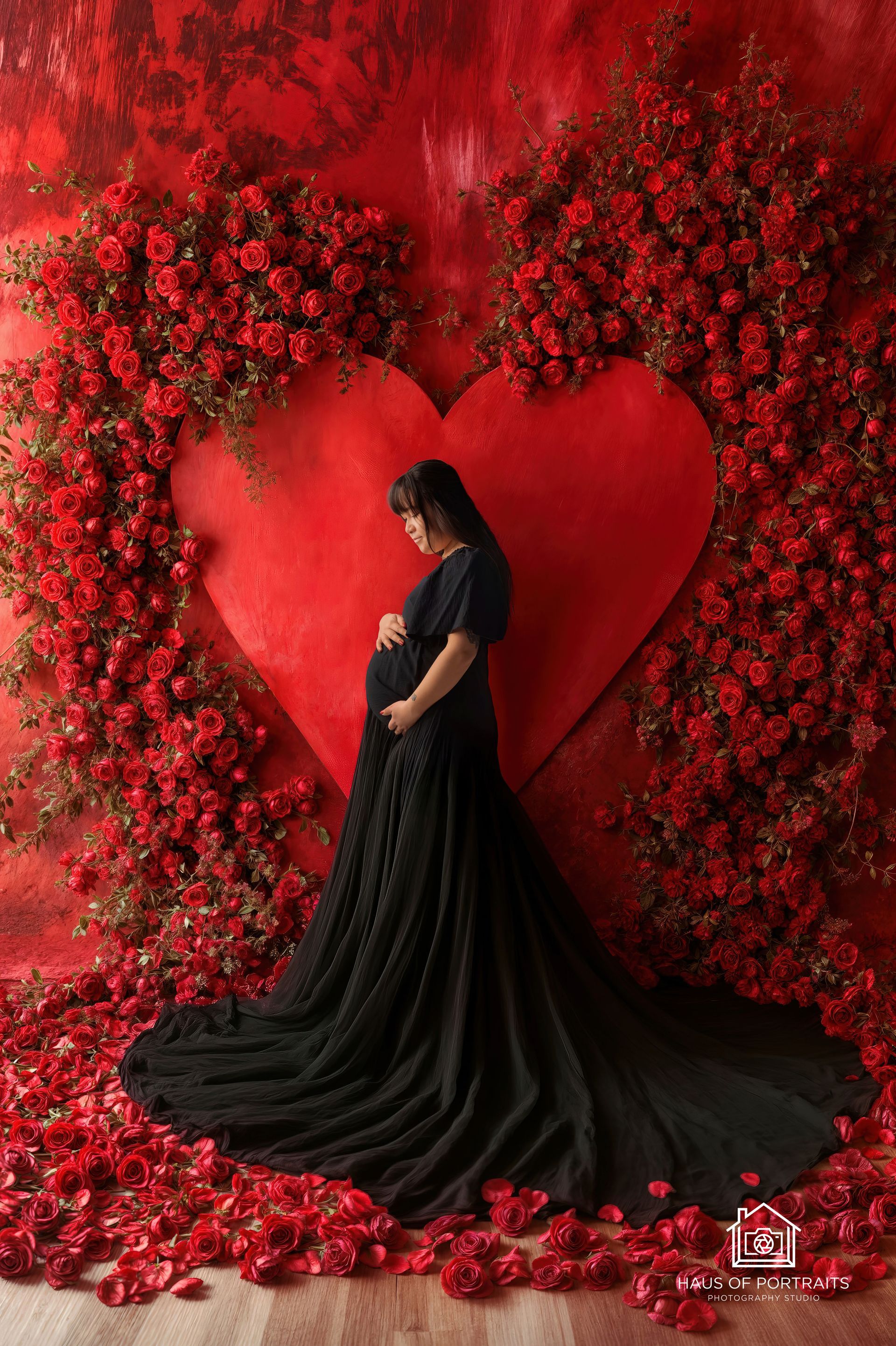 Woman in a black gown posing before a red heart-shaped floral backdrop