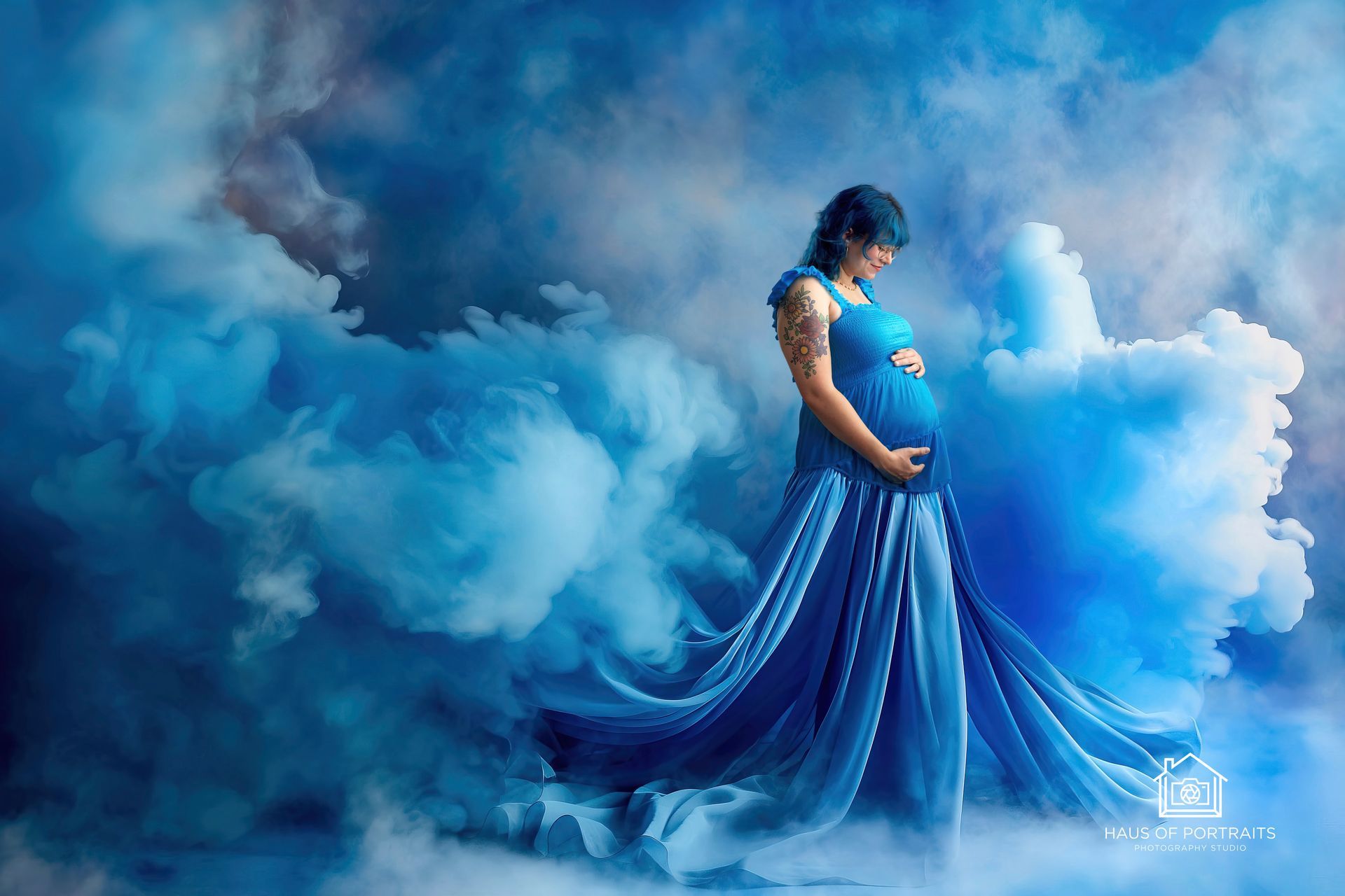 Person in a flowing blue gown standing in a cloudy blue dreamscape, looking down at their belly.