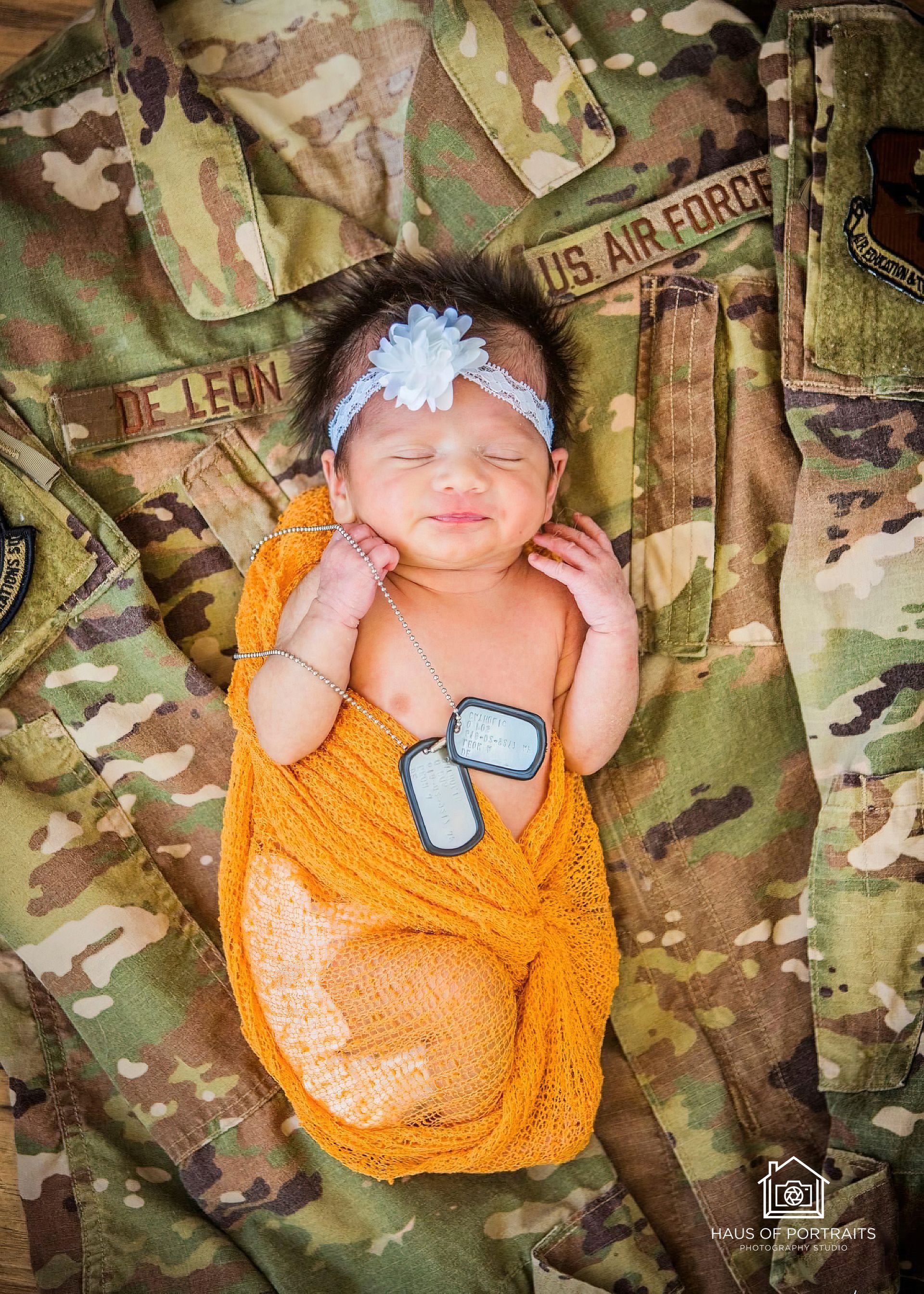 Sleeping baby in orange wrap on camouflage military uniform with a blue headband