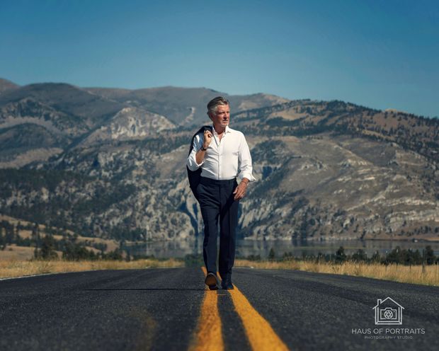 Man standing on a road with yellow lines, mountains in the background under a clear sky