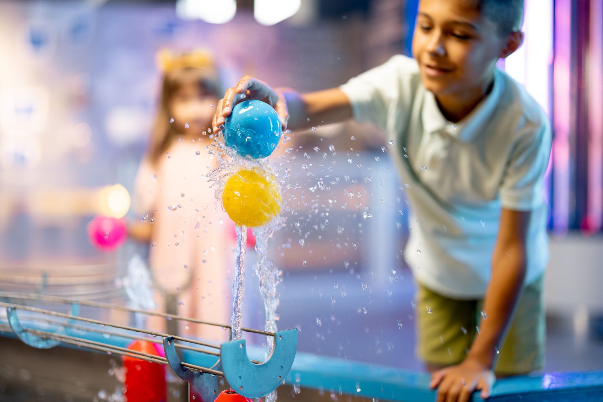Child leaning over a science table, touching colorful water bubbles with a blue scoop