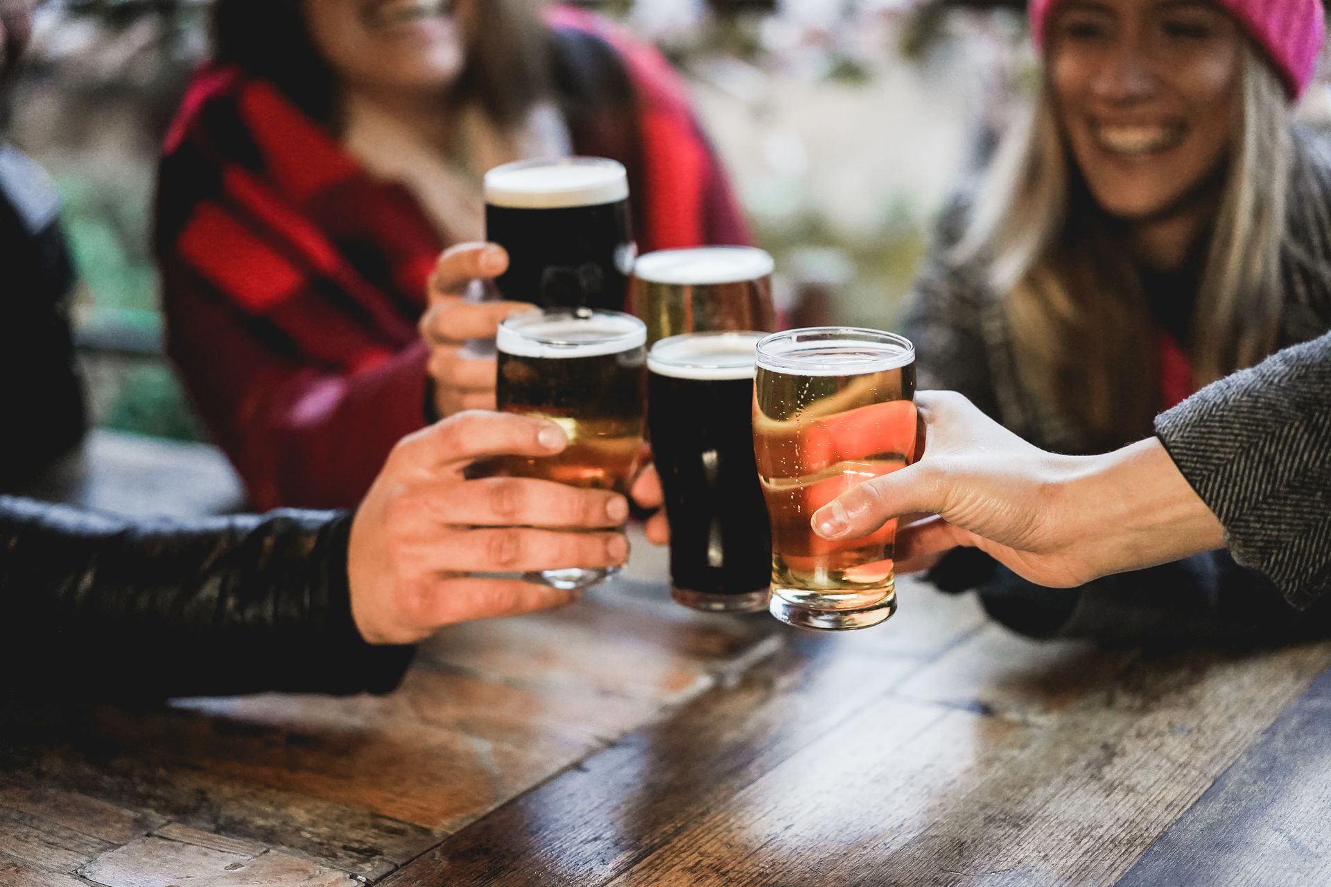 Friends toasting pints of beer at a table in a lively bar setting