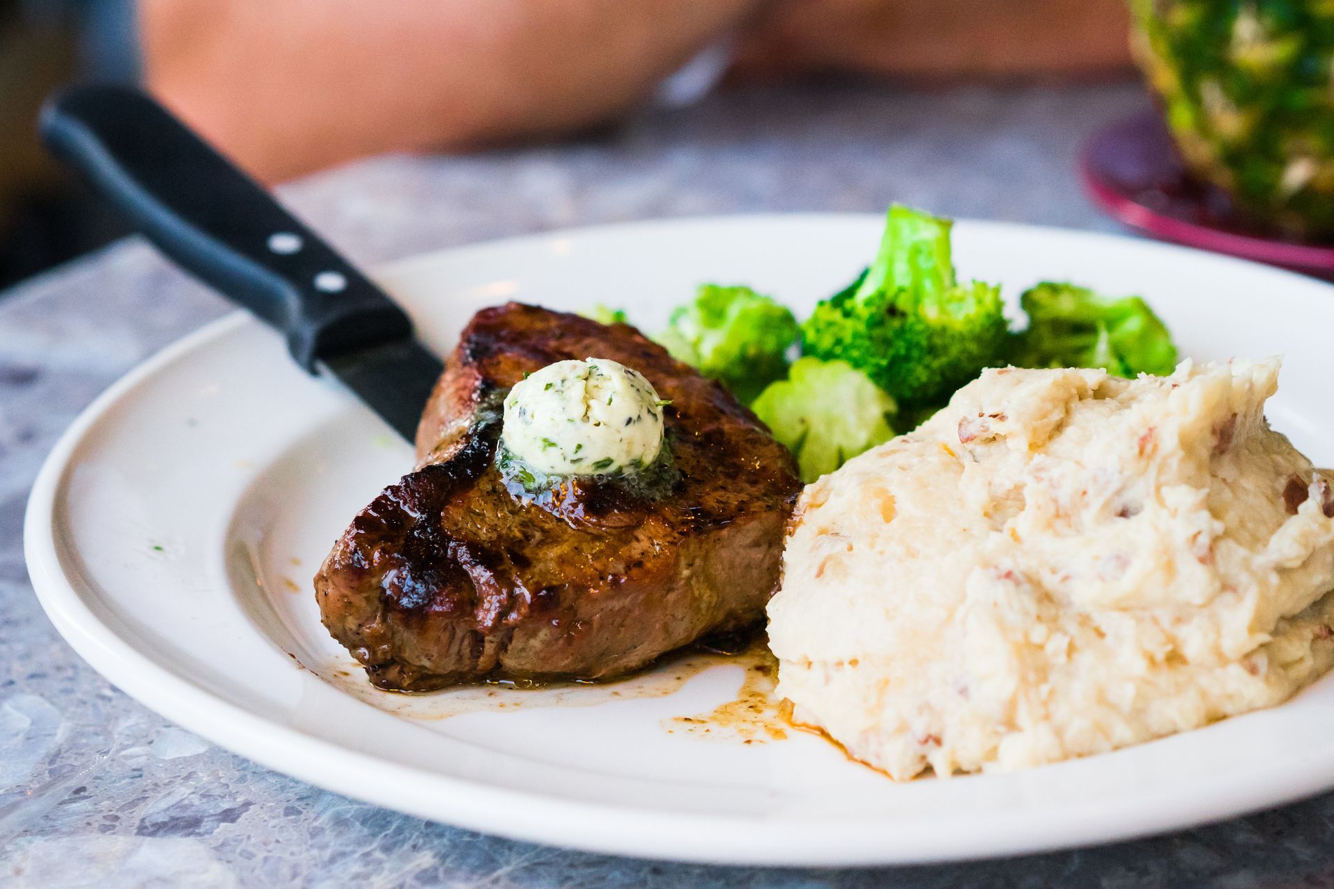 Plated steak with mashed potatoes and broccoli, topped with herb butter on a white dish