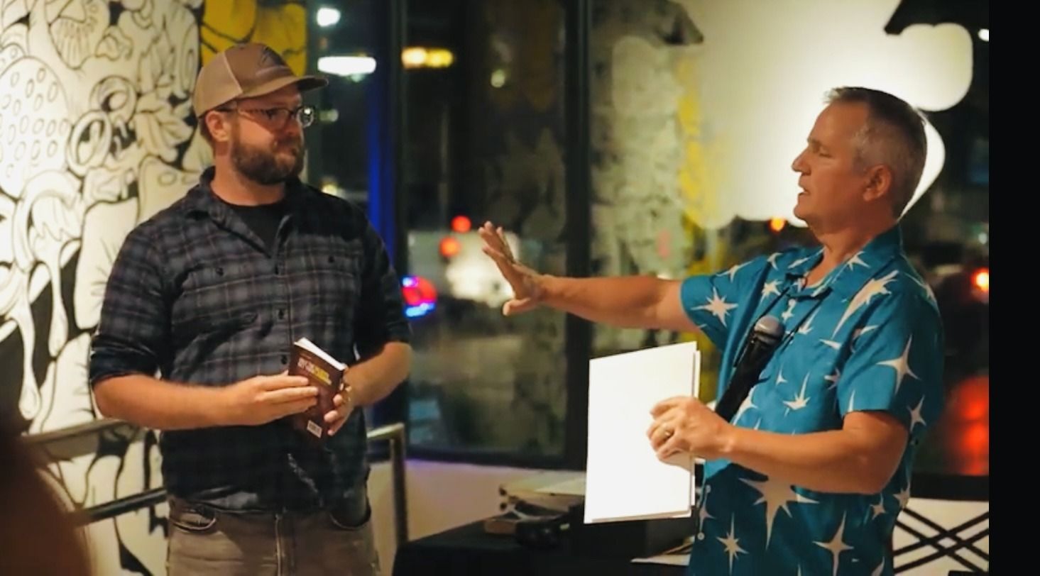 Two men are standing next to each other in a room talking to each other.