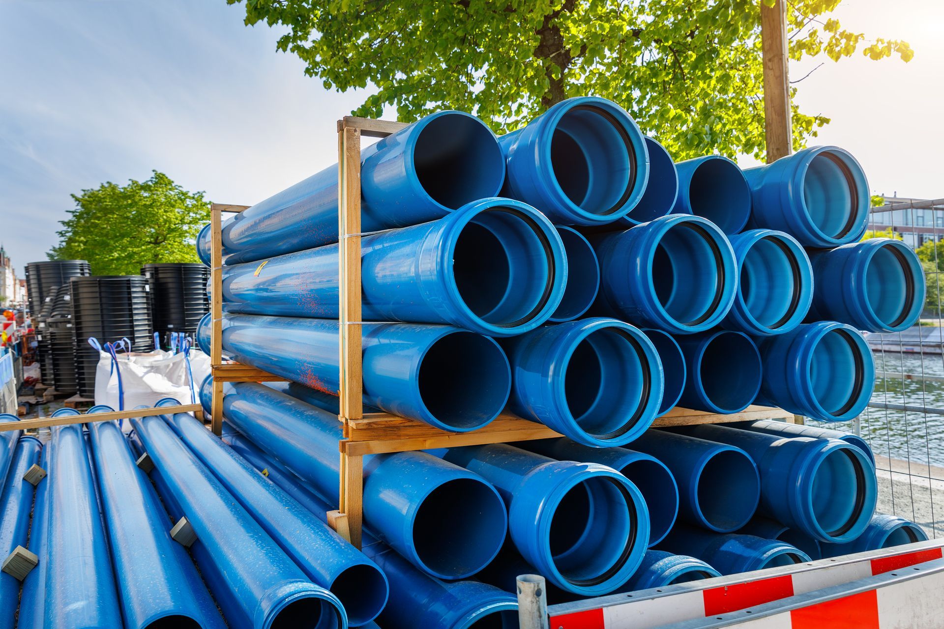 Des tuyaux en plastique bleu empilés sur des palettes en bois à l'extérieur.