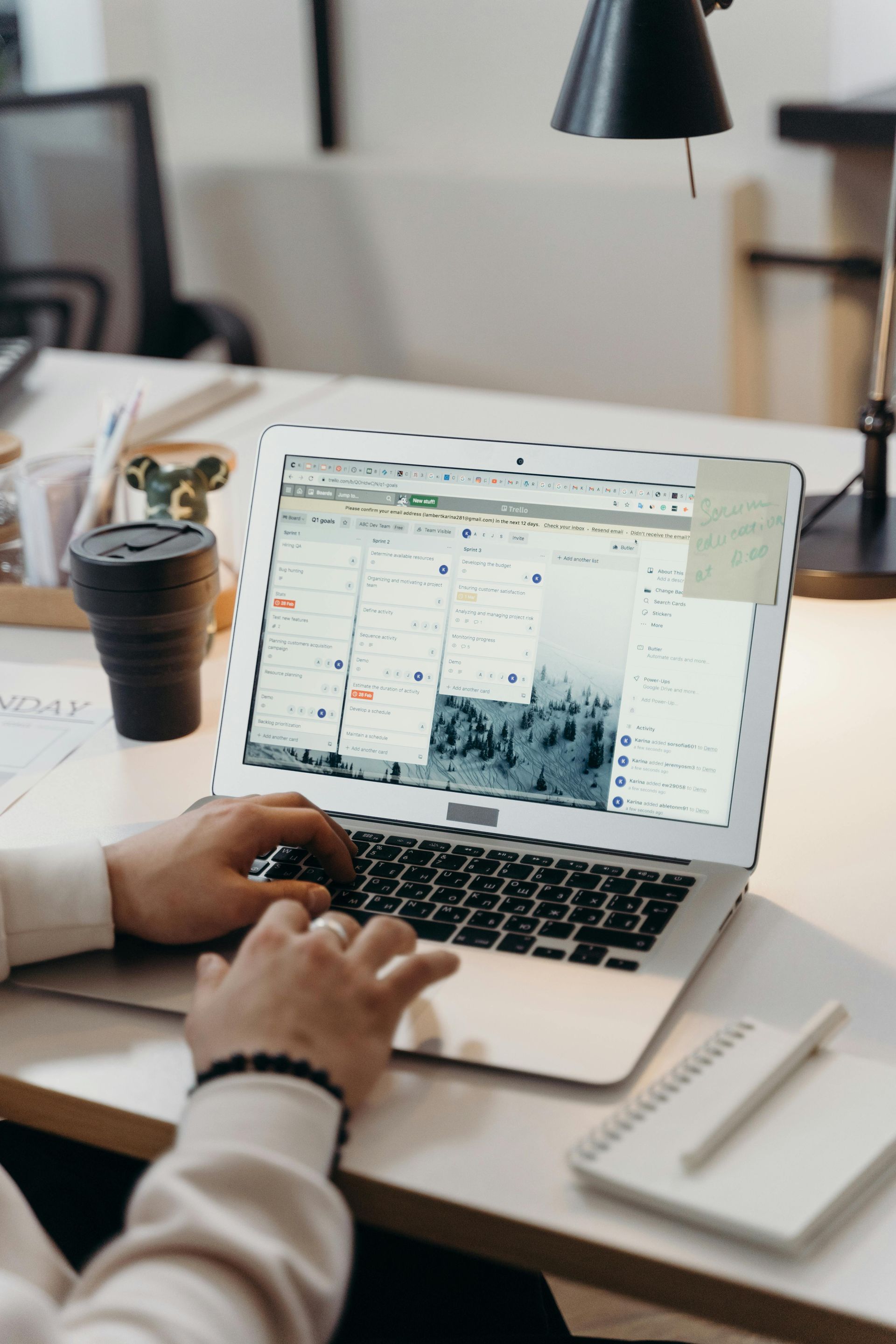 Une personne tape sur un ordinateur portable, consultant une page web avec des images, près d'un carnet et d'une tasse de café.