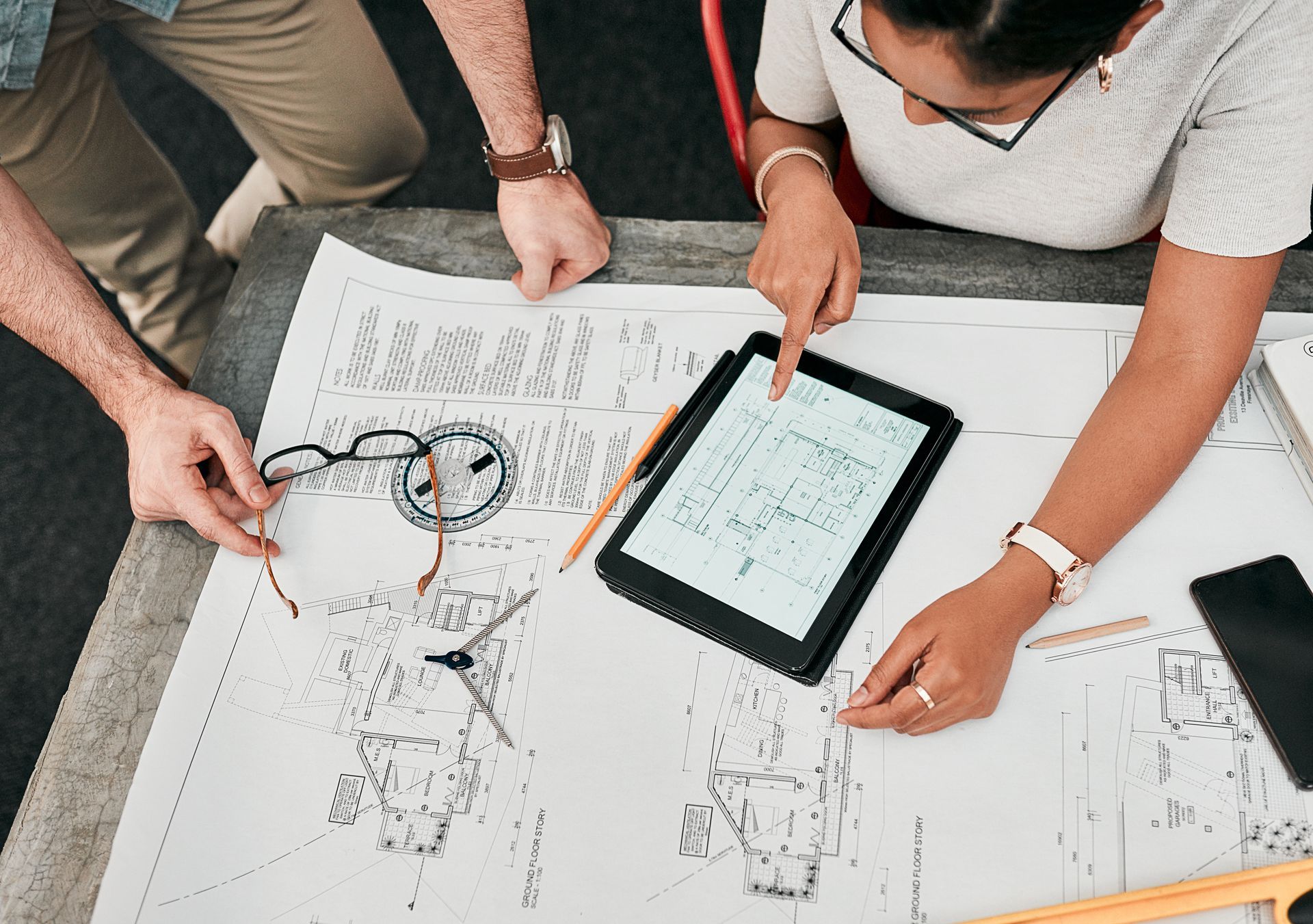 Deux personnes collaborent sur des plans architecturaux, l'une d'elles pointant du doigt une tablette, à l'intérieur.