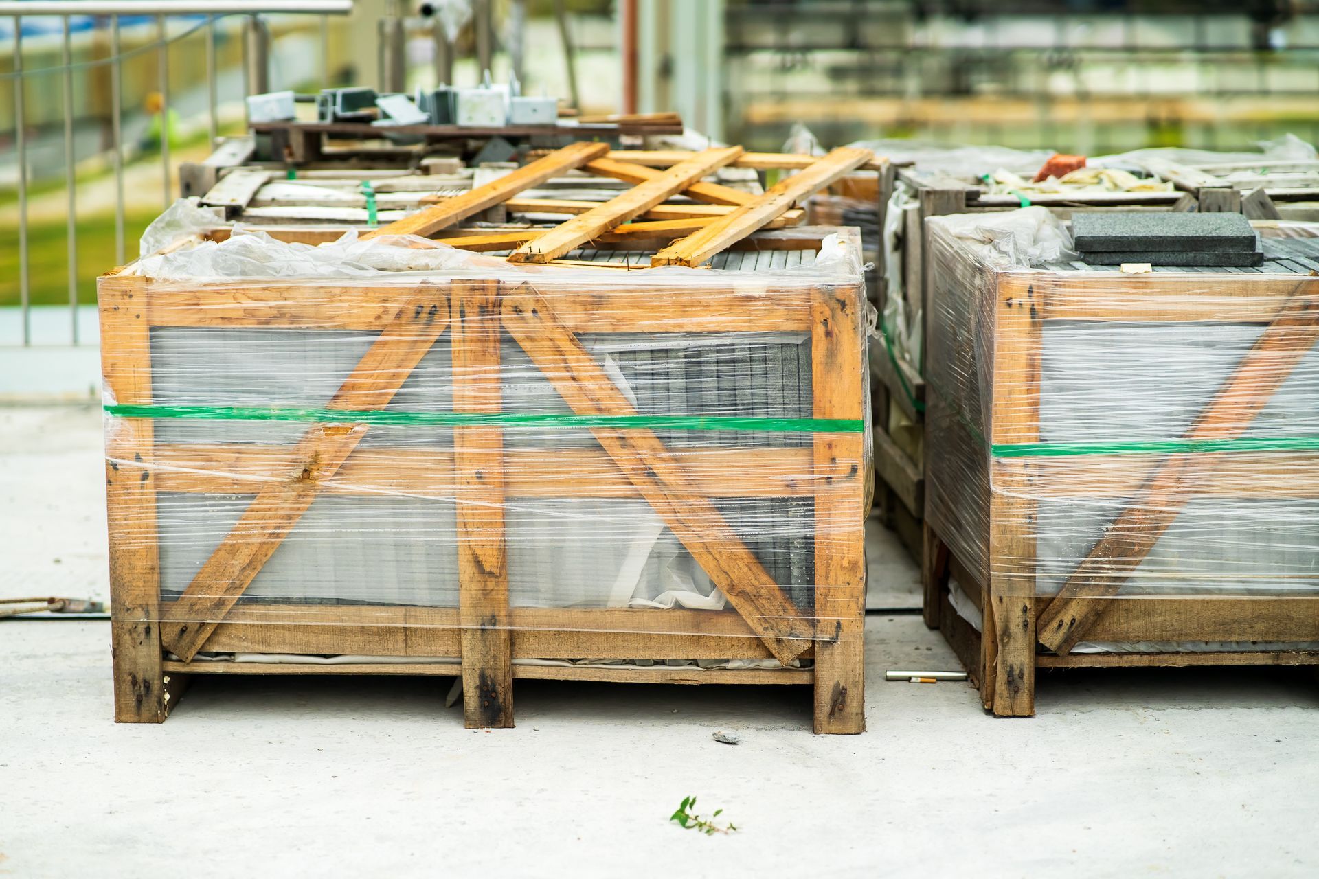 Deux caisses en bois enveloppées dans du plastique, posées sur une surface blanche, à l'extérieur.