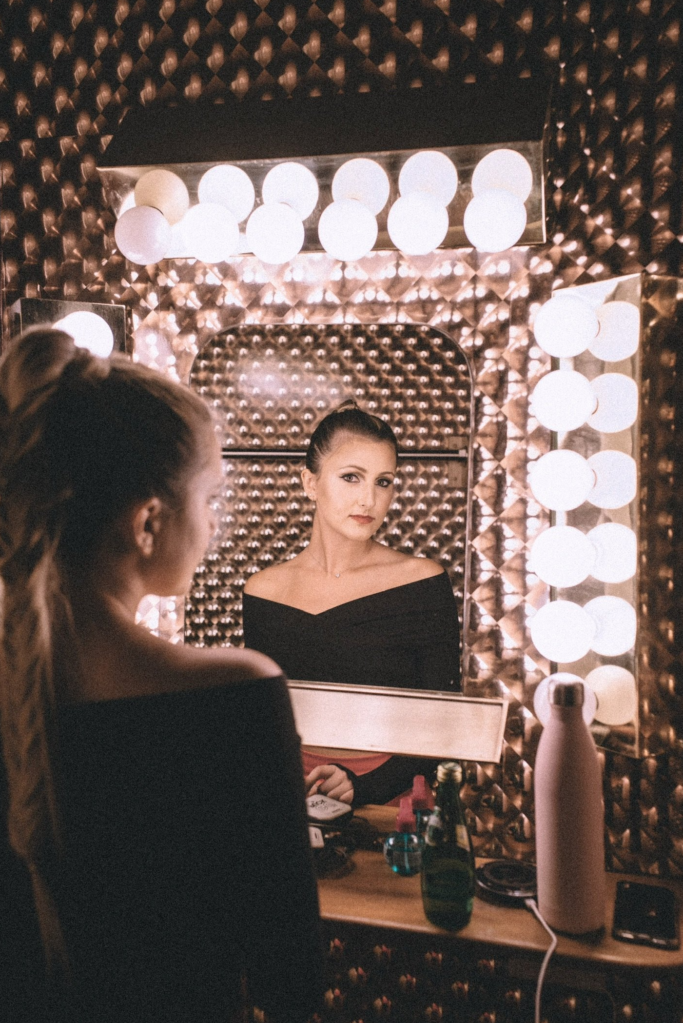 Brunette woman with high sleek ponytail looking in mirror on set