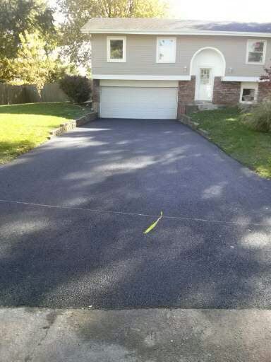 A newly paved asphalt driveway leads to a suburban split-level house with a white garage door and green lawn.