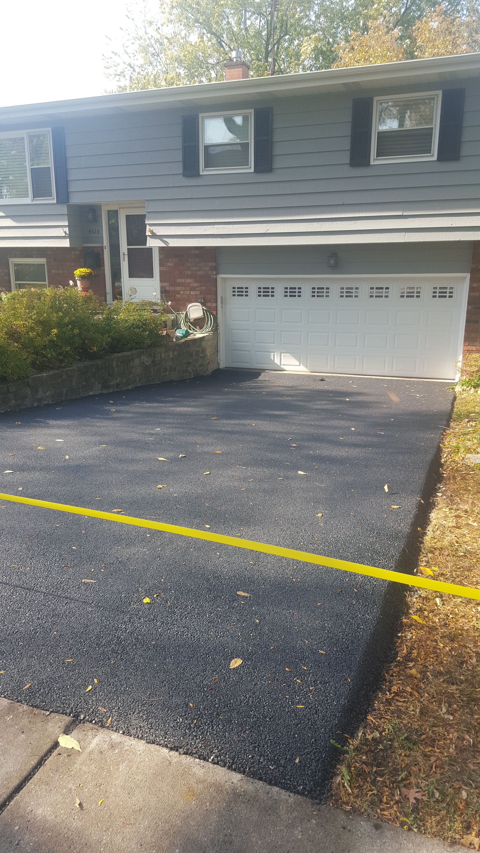 A freshly paved asphalt driveway leading to a house with a white garage door, marked off by a yellow caution tape.
