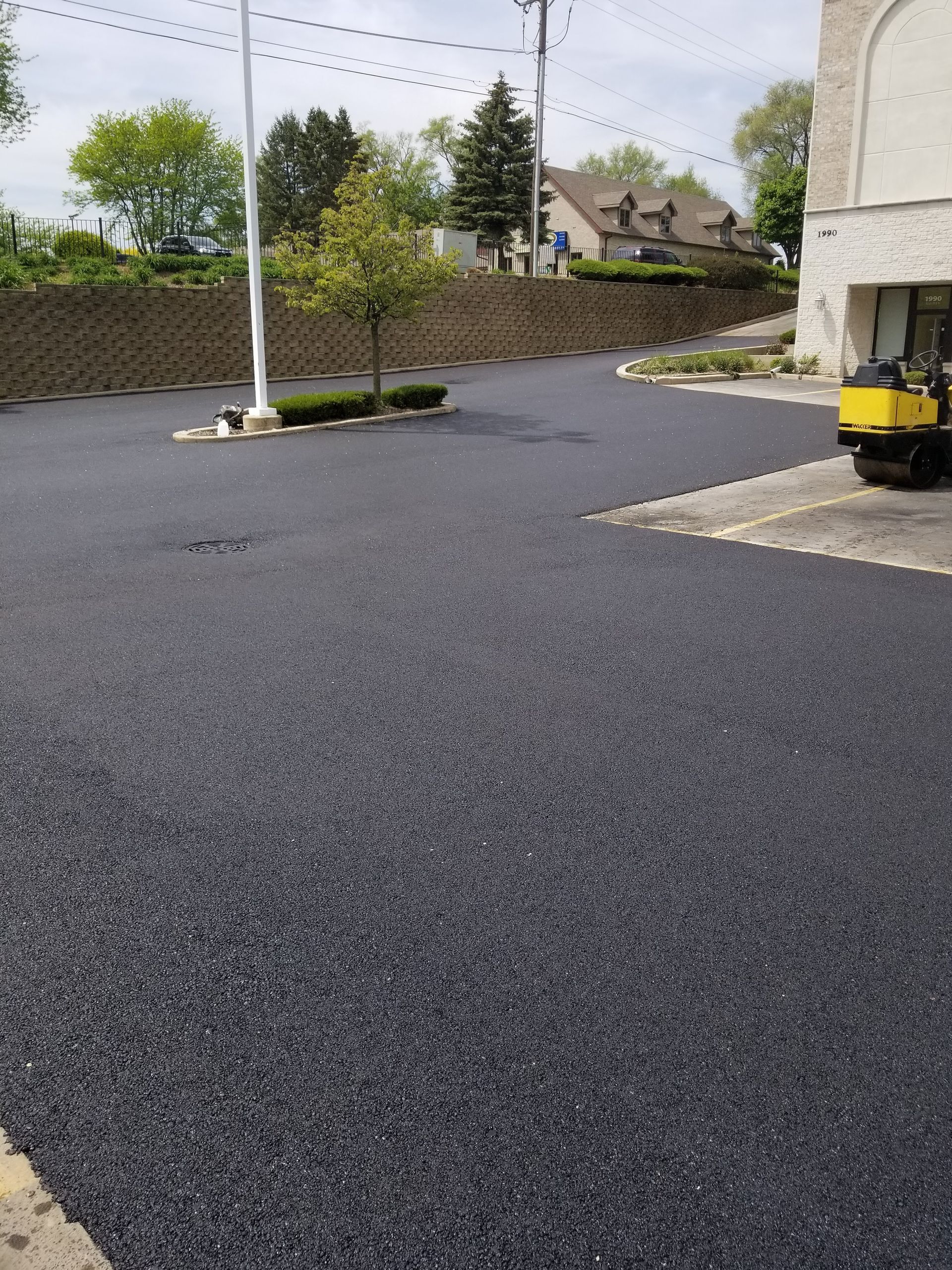 A freshly paved asphalt parking lot on a sunny day with a small yellow roller vehicle nearby.