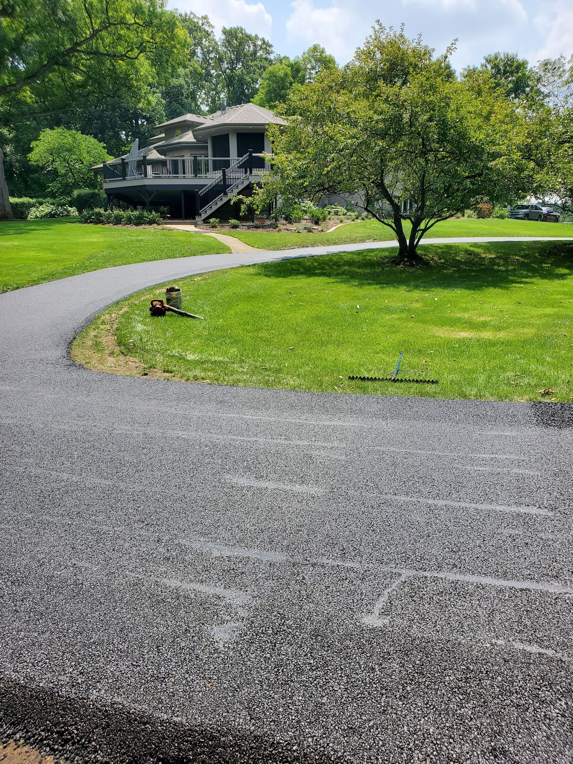 A freshly paved, dark gray gravel path curves through a green lawn toward a large house in the background.