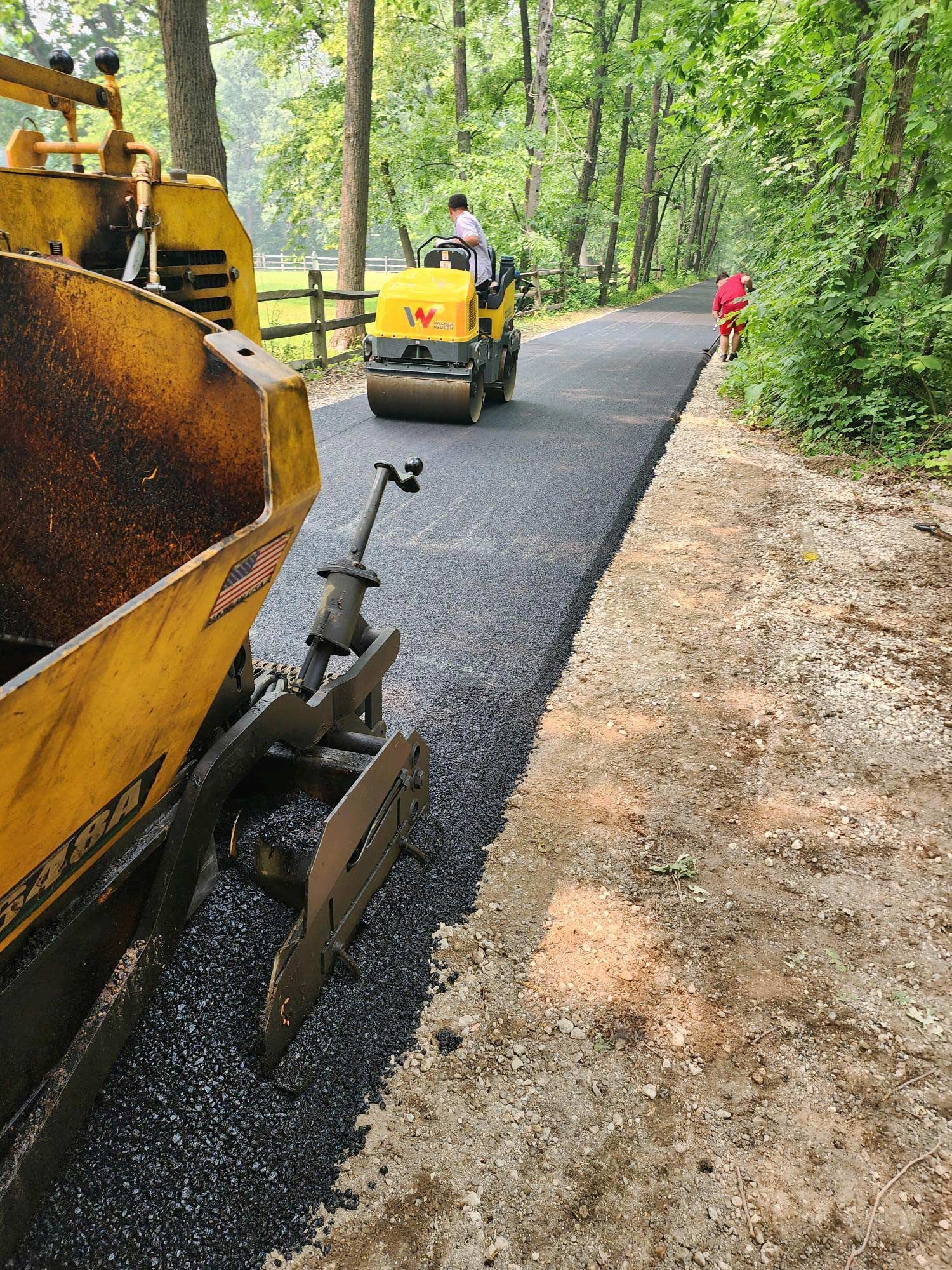 A skid steer loader and construction workers in high-visibility gear remove old pavement from a residential driveway.