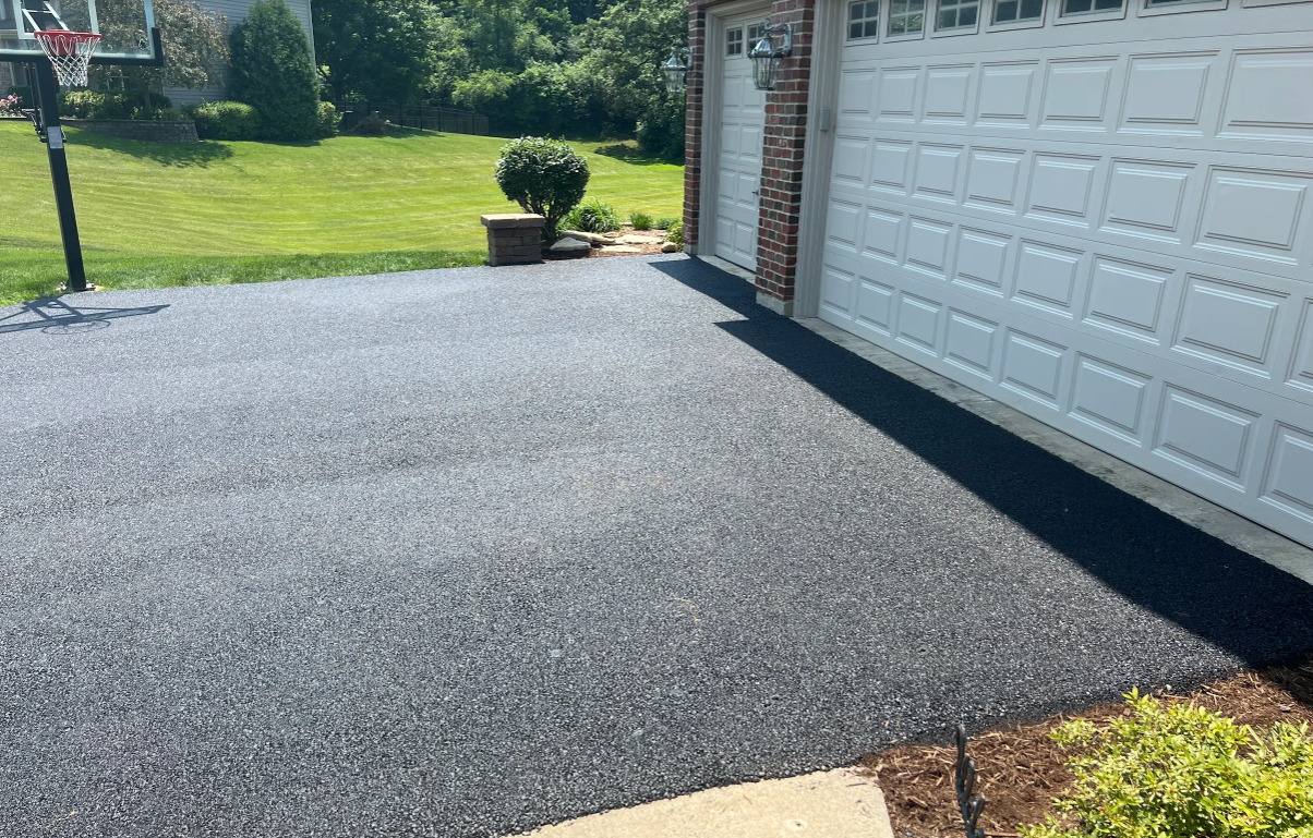 A freshly paved asphalt driveway leading to a white two-car garage next to a grassy lawn.