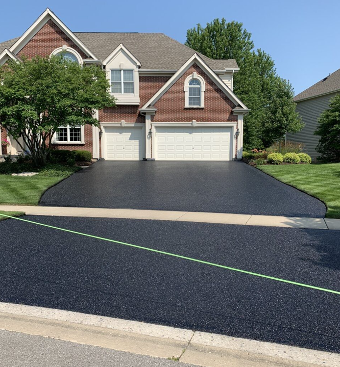A brick house with a newly paved asphalt driveway and a green surveyor's string line across the foreground.