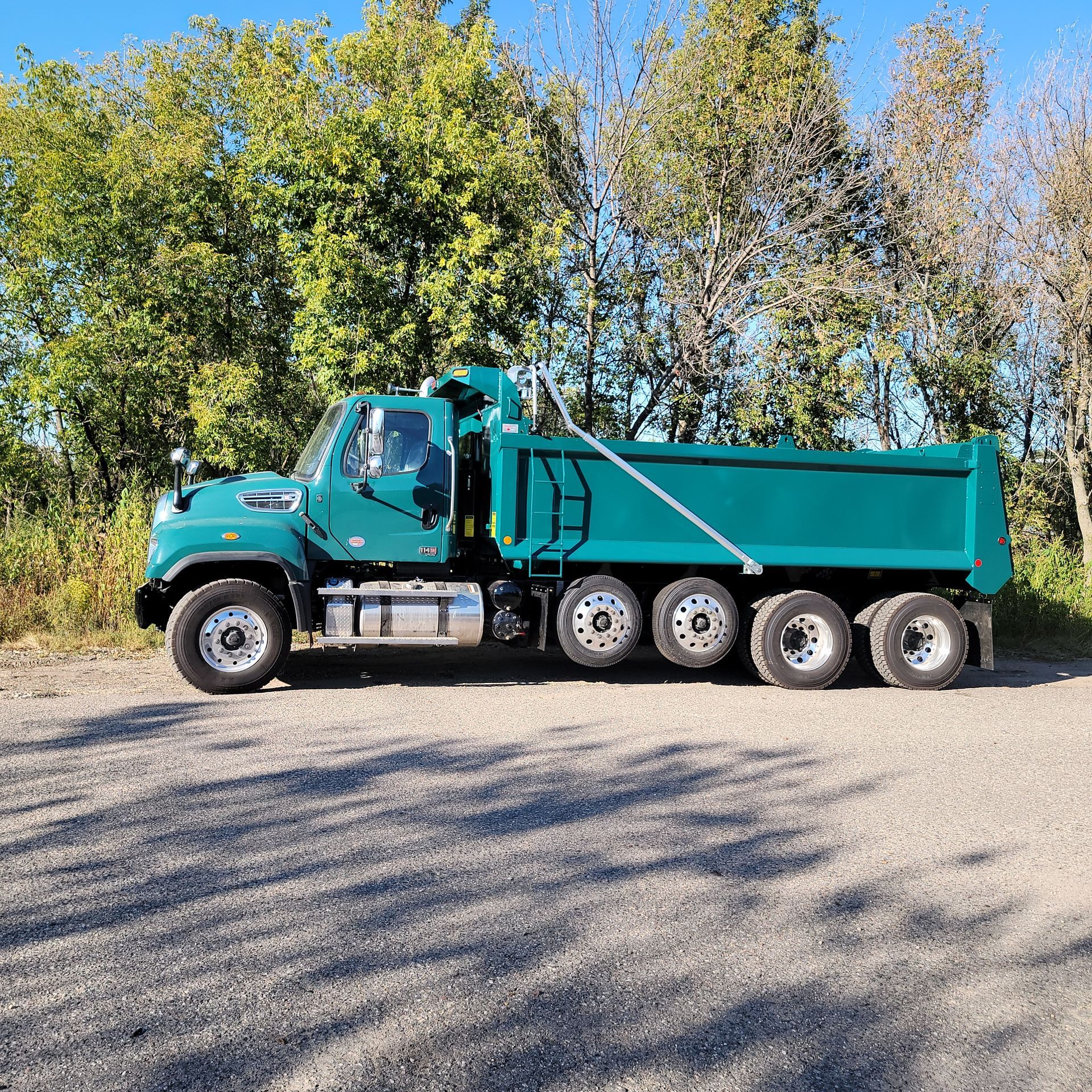 A blue dump truck is parked on a gravel road.