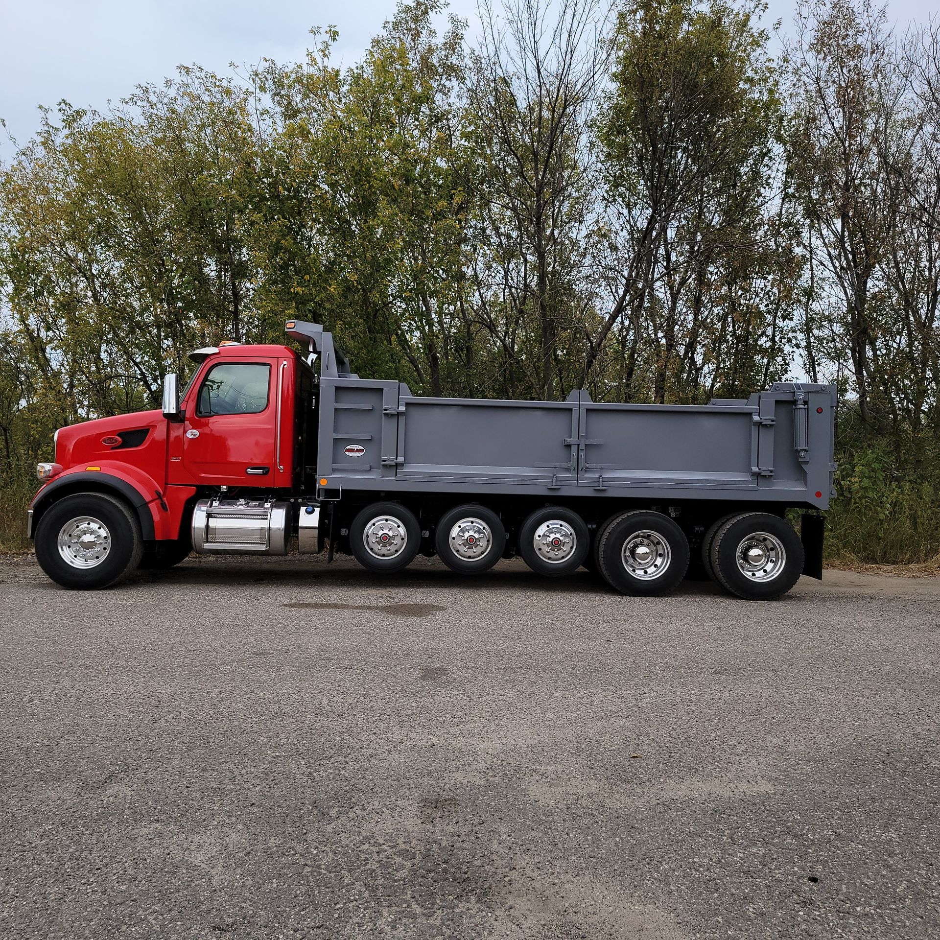 A red dump truck is parked in a gravel lot