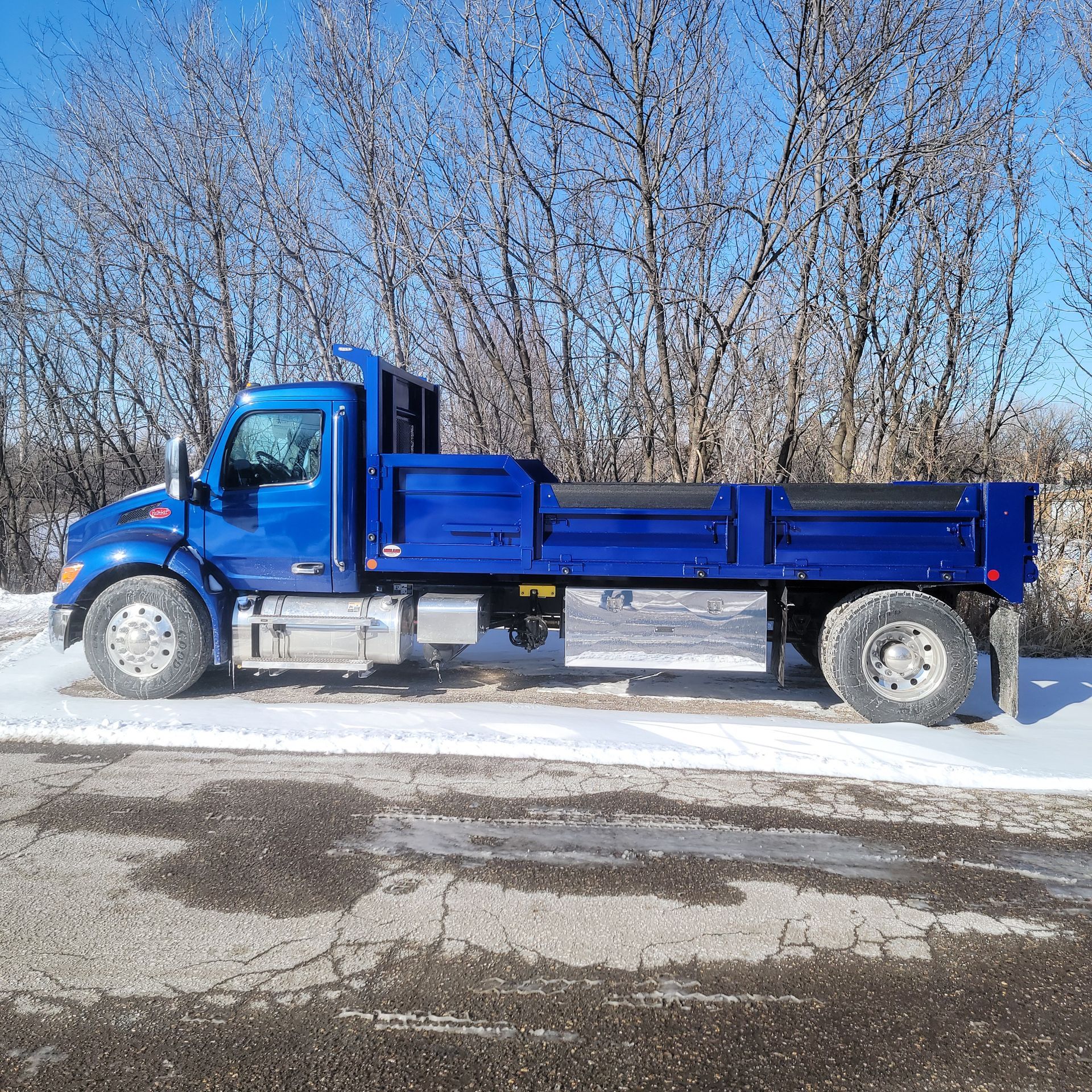 A blue dump truck is parked on the side of the road in the snow.