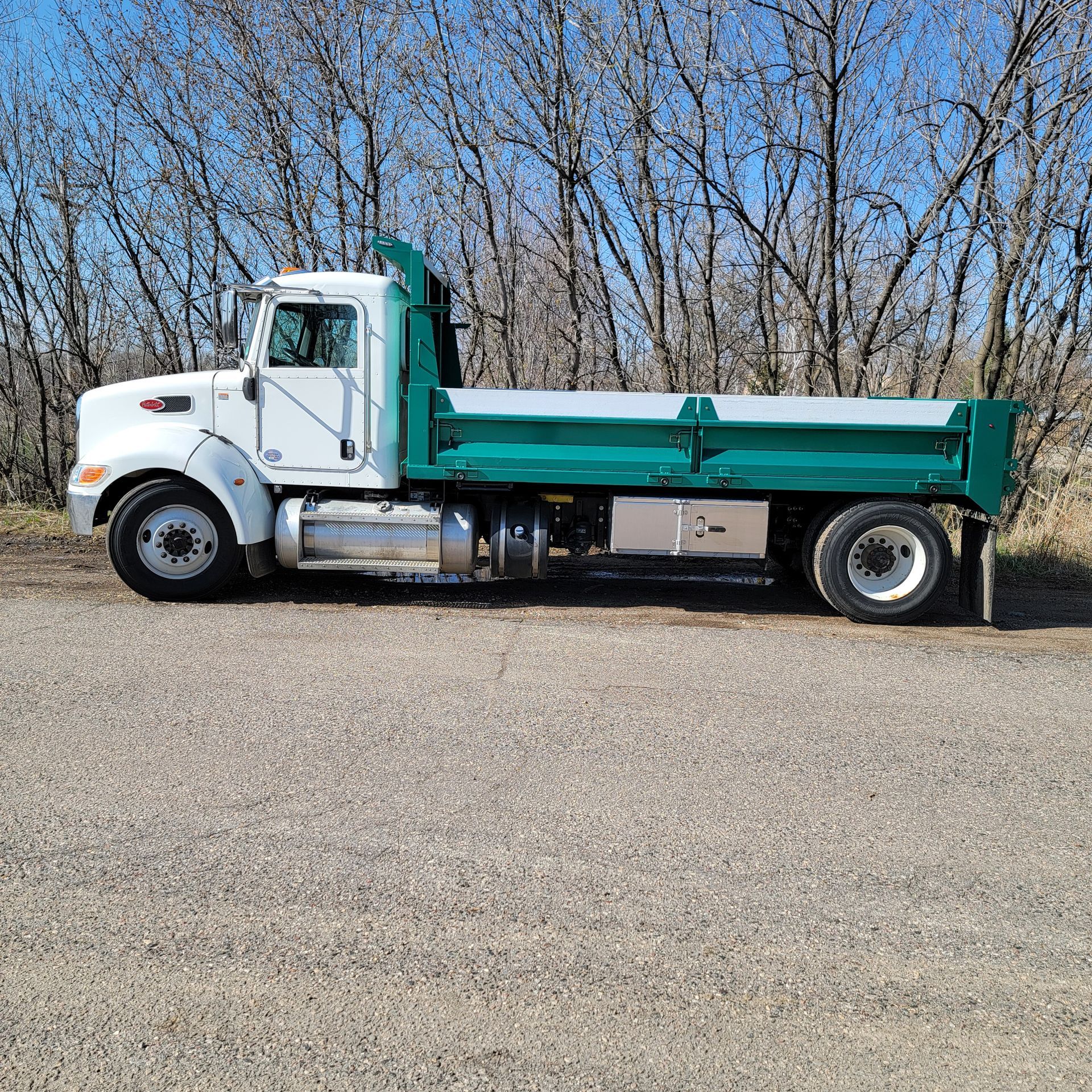 A white dump truck with a green bed is parked on the side of the road.