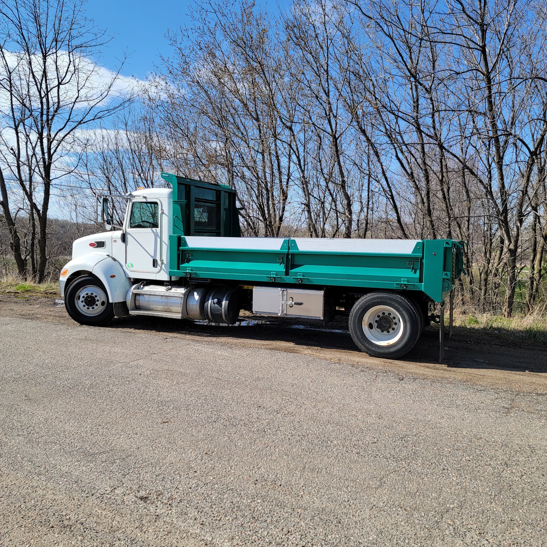 A white and green dump truck is parked on the side of the road.