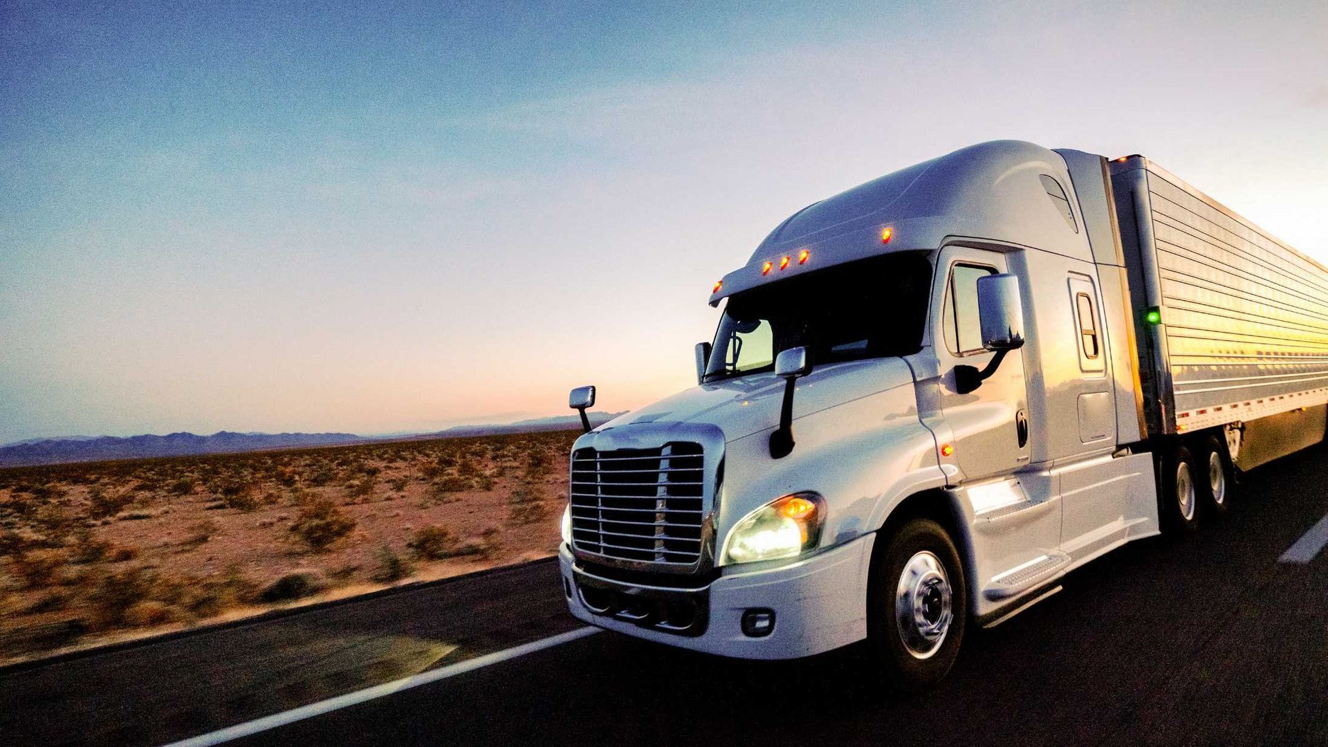 A semi truck is driving down a highway in the desert.