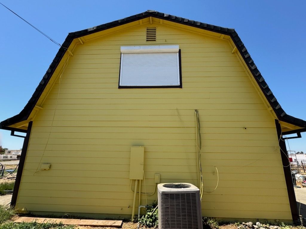 Yellow barn with black trim and a white window on a sunny day.