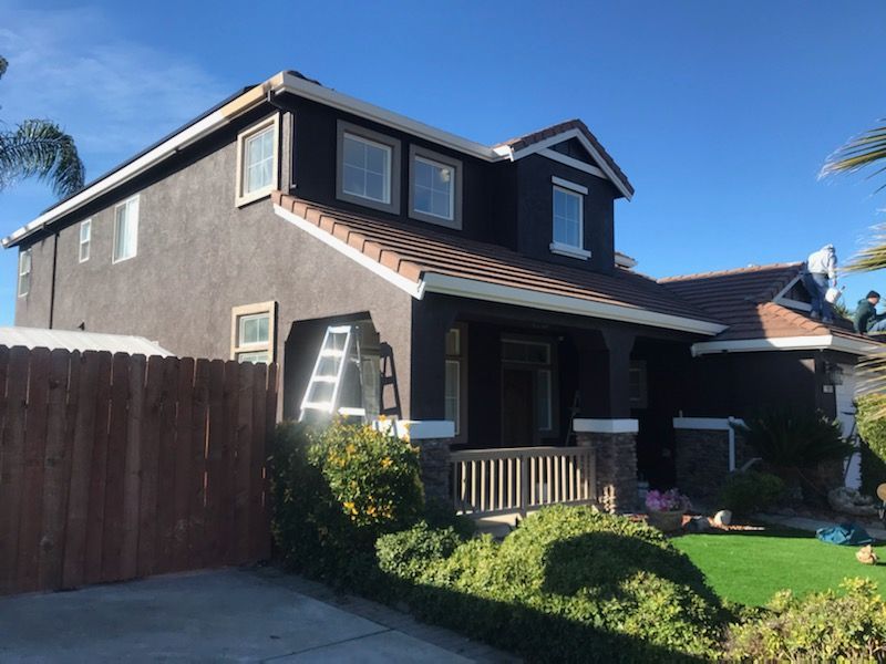 Two-story brown house with white trim, wooden fence, and green lawn on a sunny day.