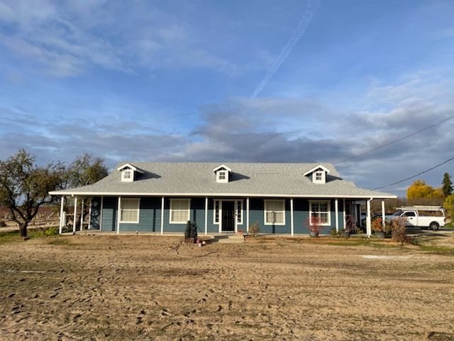 Blue ranch house with a long porch, set in a dry field under a cloudy sky.