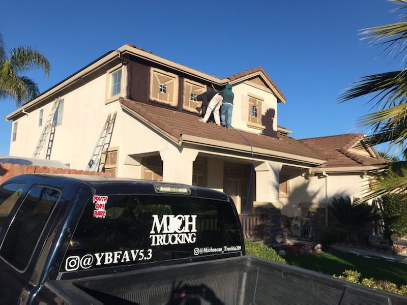 Two people on a roof of a two-story beige house. Black truck in front.