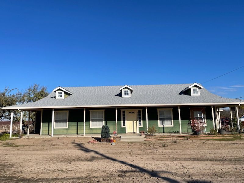 Green house with long porch, gray roof, three dormers, blue sky.
