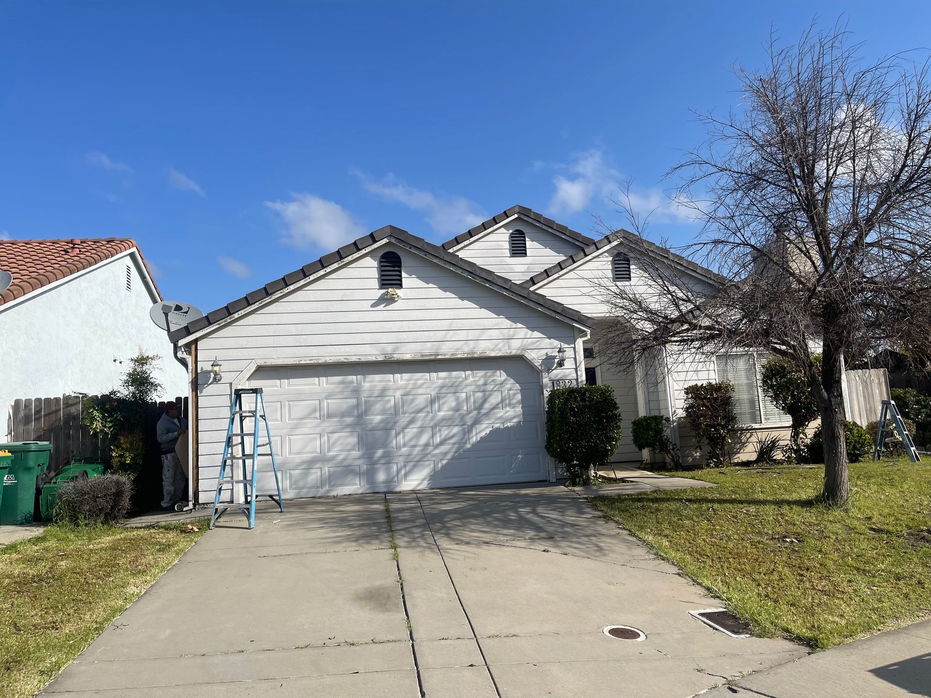 White house with a two-car garage and driveway on a sunny day. Ladder leans against the garage.