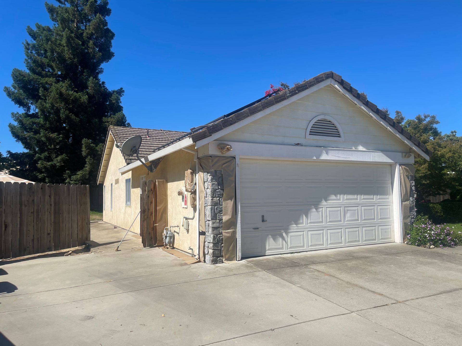 Garage with white door, beige walls, stone accents, and a tile roof under a blue sky.