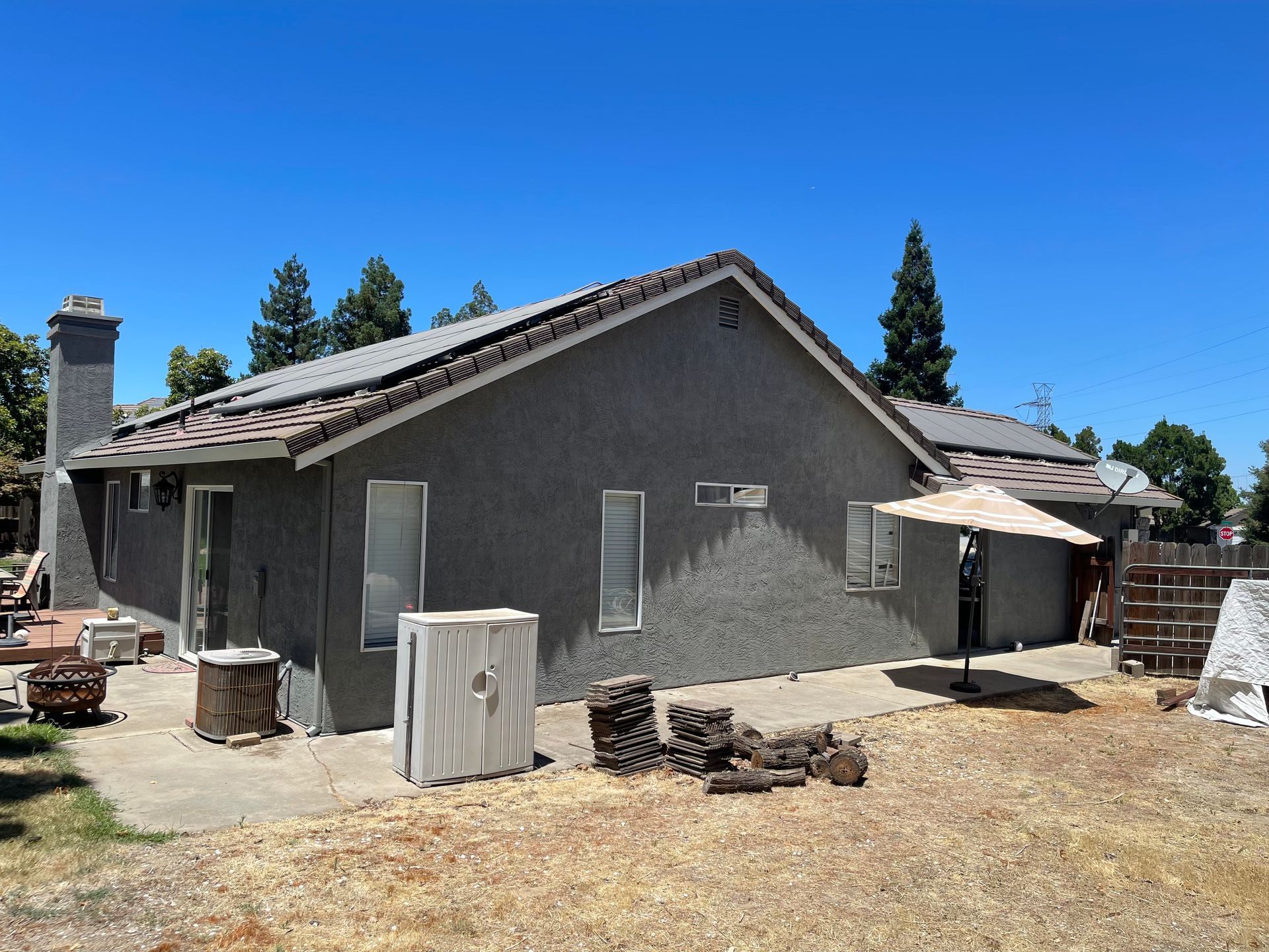 Gray house with a tile roof, a patio umbrella, and a dry, sunny backyard.