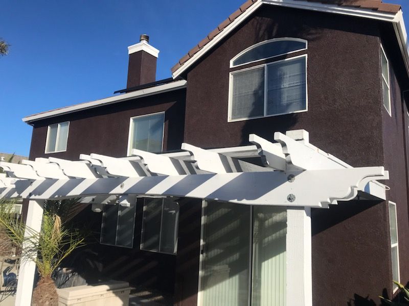 Brown house with white pergola, windows, and chimney against a bright blue sky.