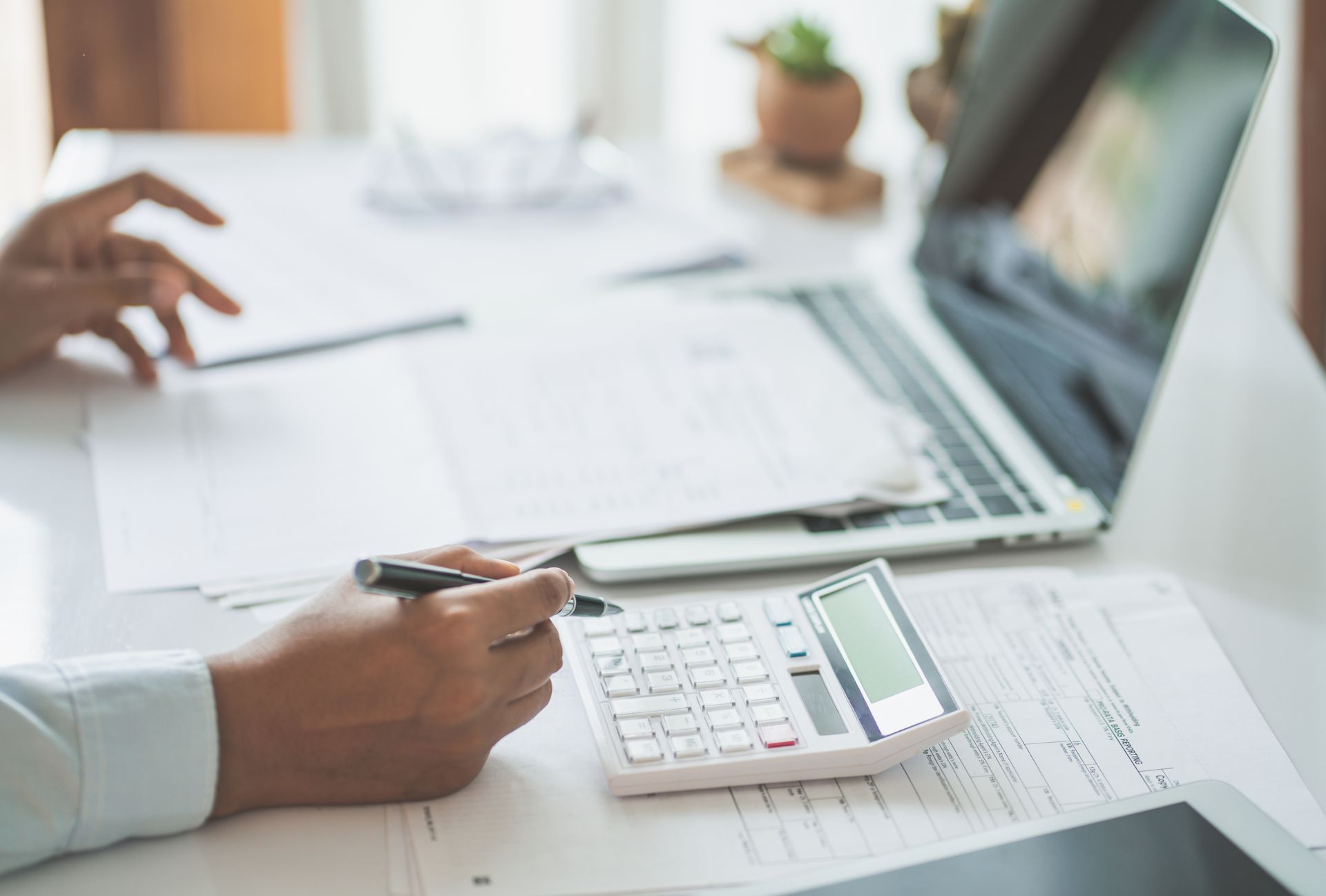A close-up of hands using a calculator and pen, analyzing finances for a debt settlement. A close-up of hands using a calculator and pen, analyzing finances for a debt settlement.