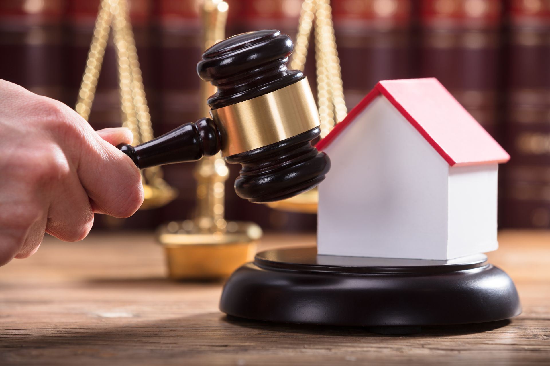 Hand striking wooden gavel on miniature house, representing chapter 7 bankruptcy.